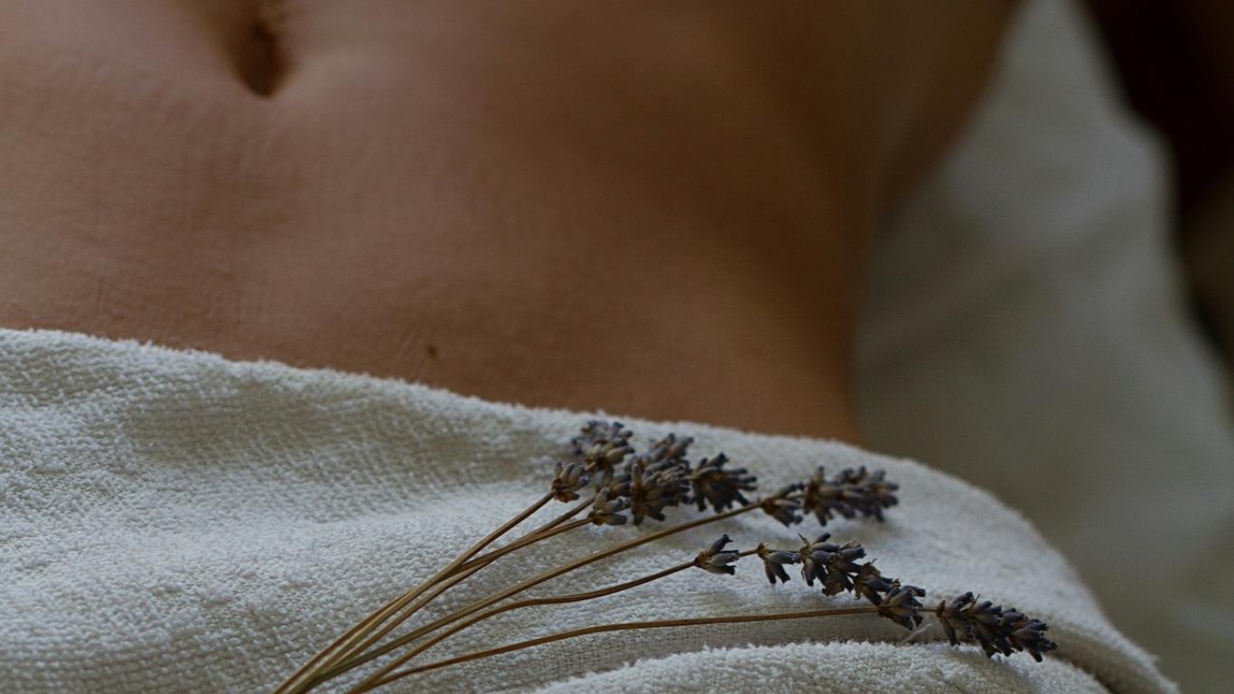 Close-up d'un ventail de lavande posé sur une nappe blanche à côté d'une partie nue du corps humain.