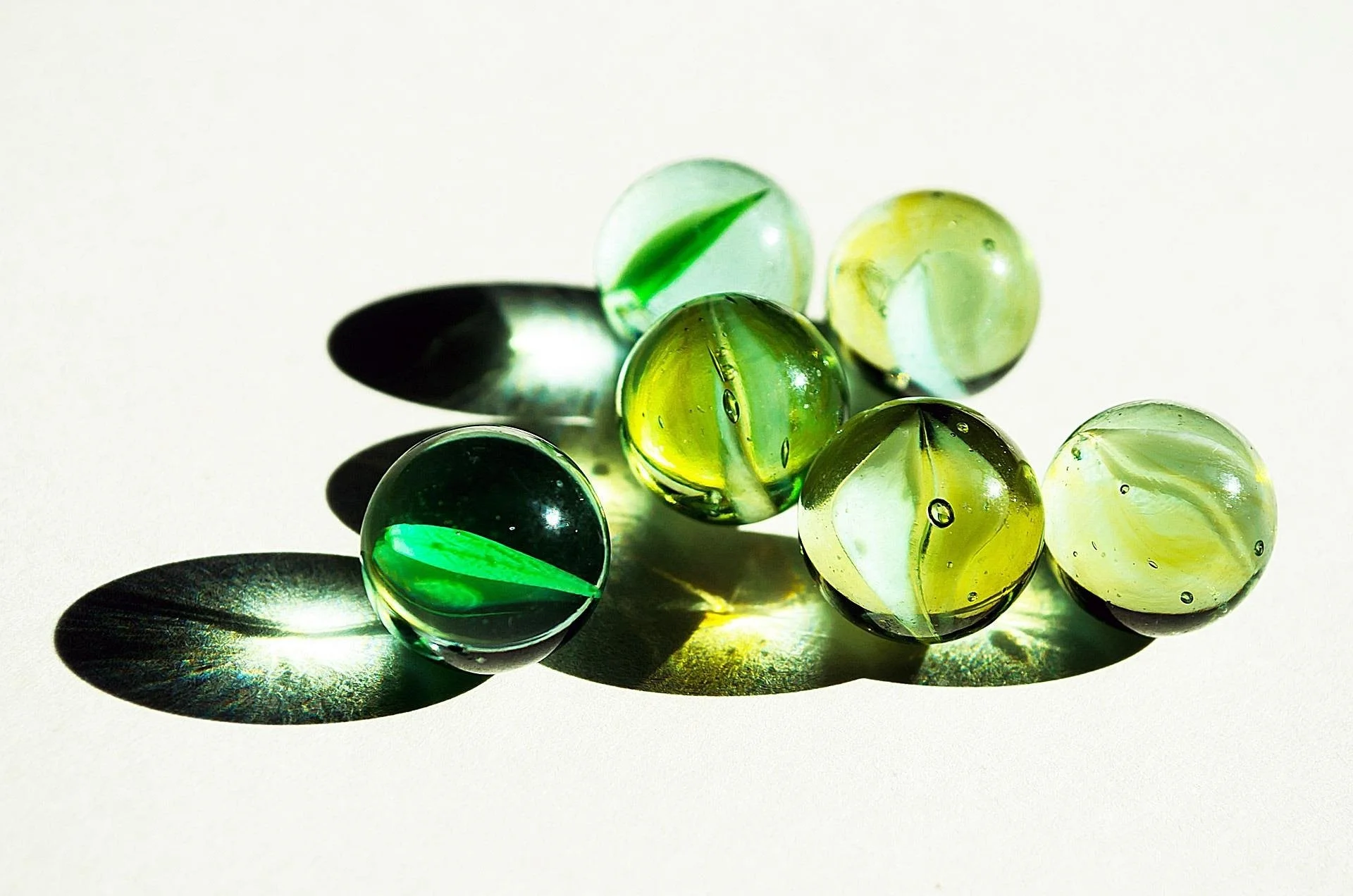 Close-up of green and yellow marbles with shadows and reflections on a white surface.