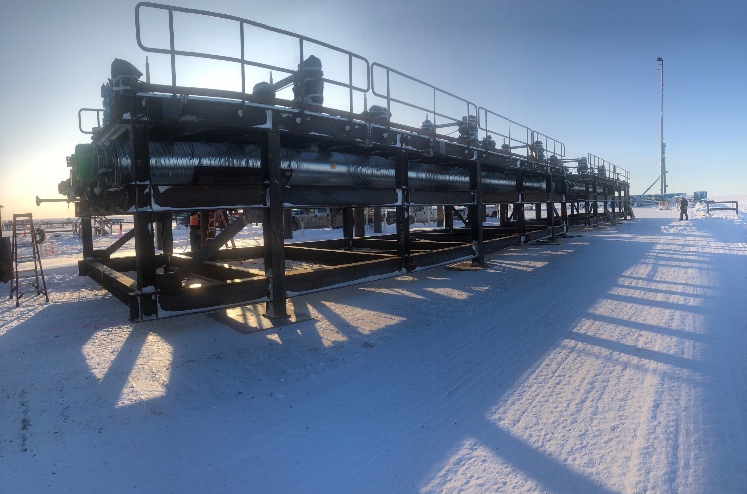 Large industrial equipment with piping and safety railings on snow-covered ground at sunset or sunrise, with a person in the distance.