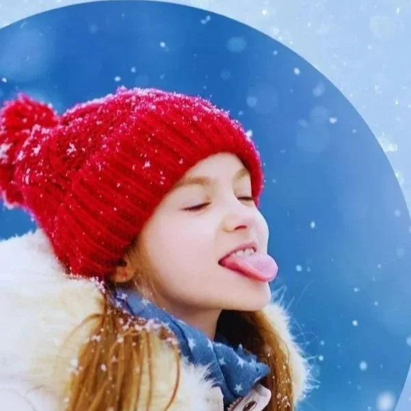 Girl wearing a red knit hat with pom-pom, sticking out her tongue in a snow scene.
