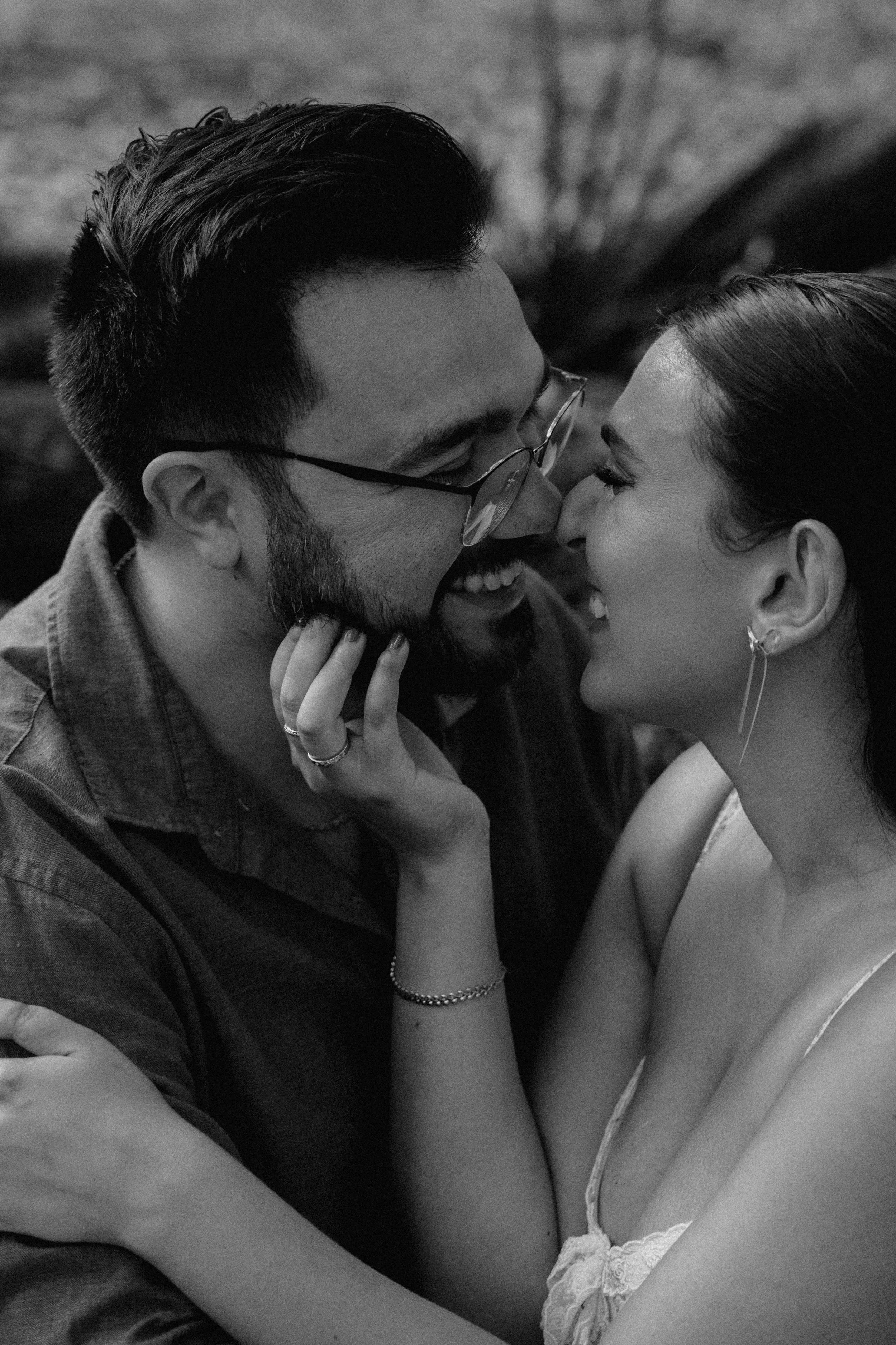 A black and white photo of a smiling couple in an intimate moment, face to face, with noses touching and eyes closed.