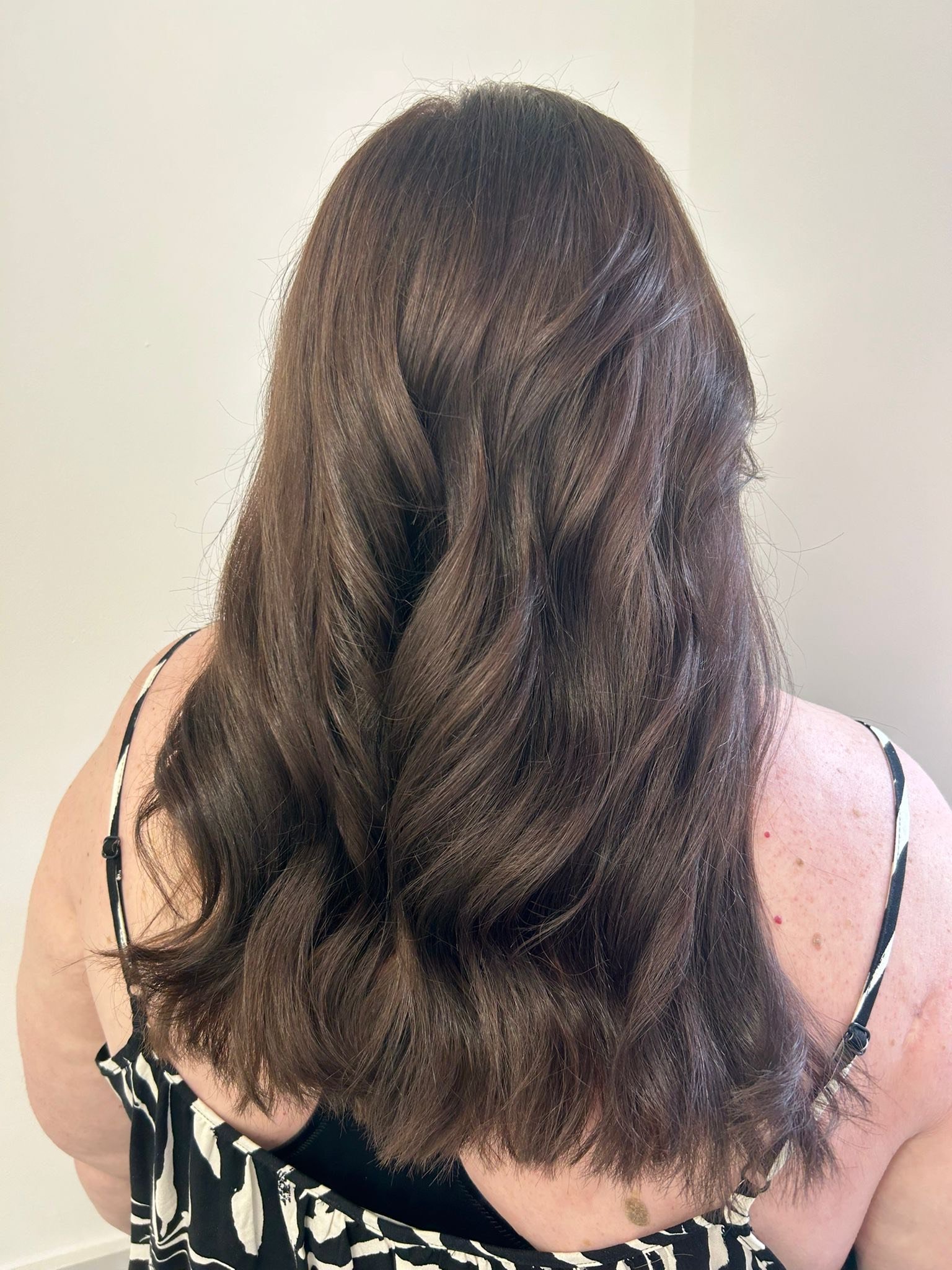 Back view of a woman with long, wavy, brown hair wearing a black and white striped top with thin straps.