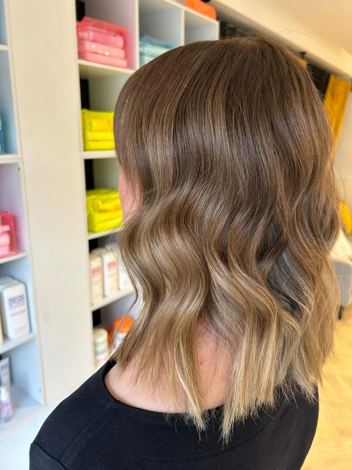 A woman with shoulder-length, wavy, light brown hair standing in front of organized shelves.