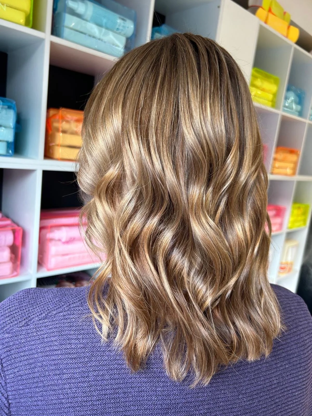 Back of a person with wavy, shoulder-length blonde hair, standing in front of a white shelving unit with colorful storage boxes.