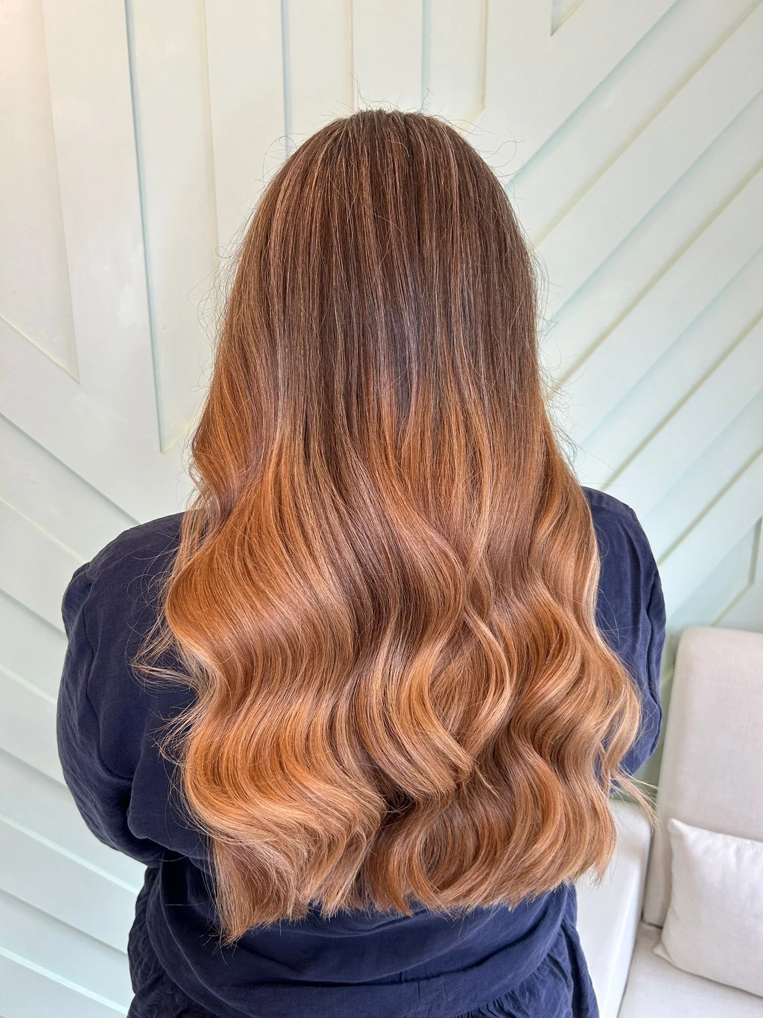 Back view of a woman with long, wavy, reddish-brown hair, wearing a dark shirt.