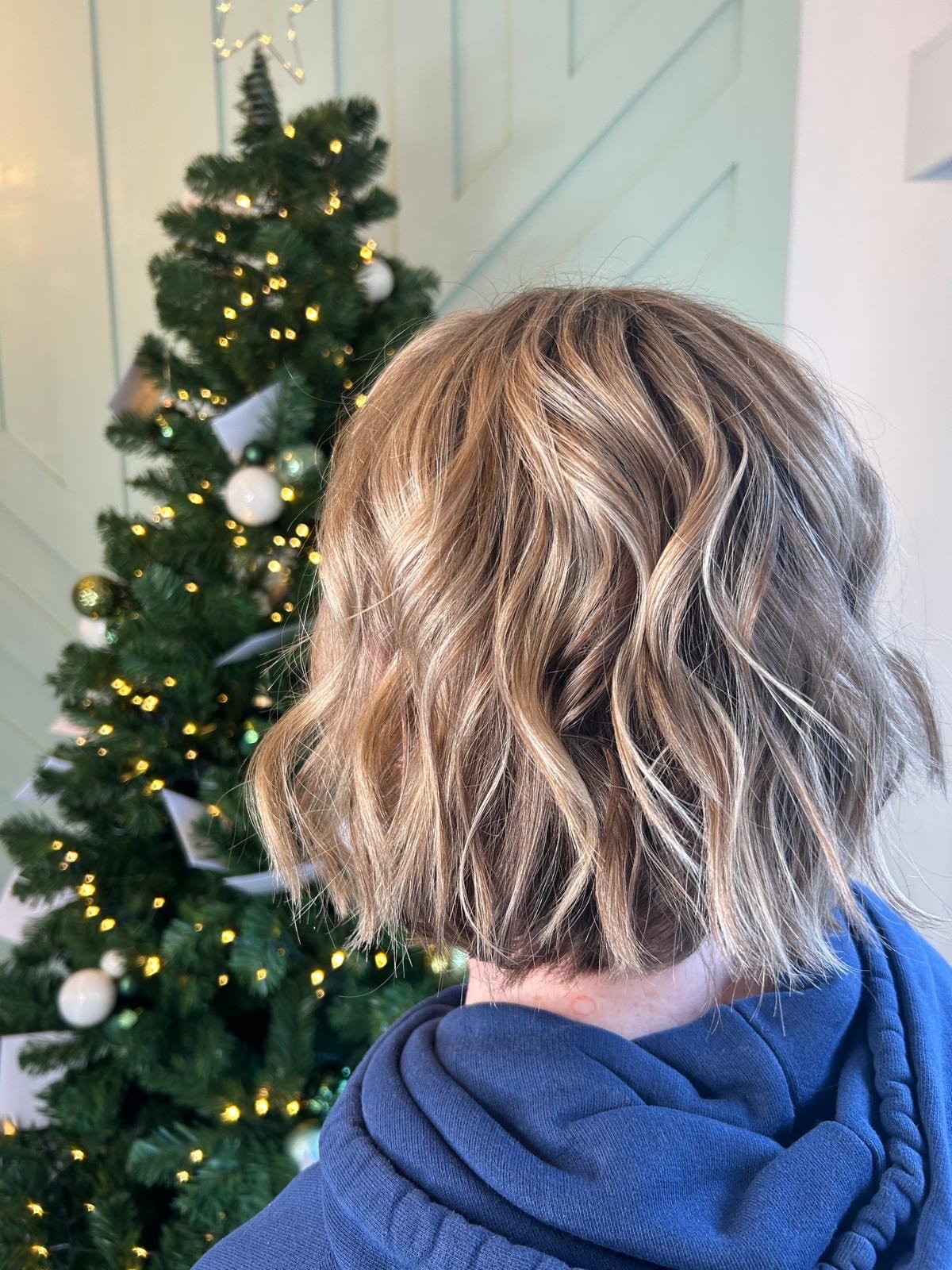 Back of a person with short, wavy blonde hair in front of a decorated Christmas tree.
