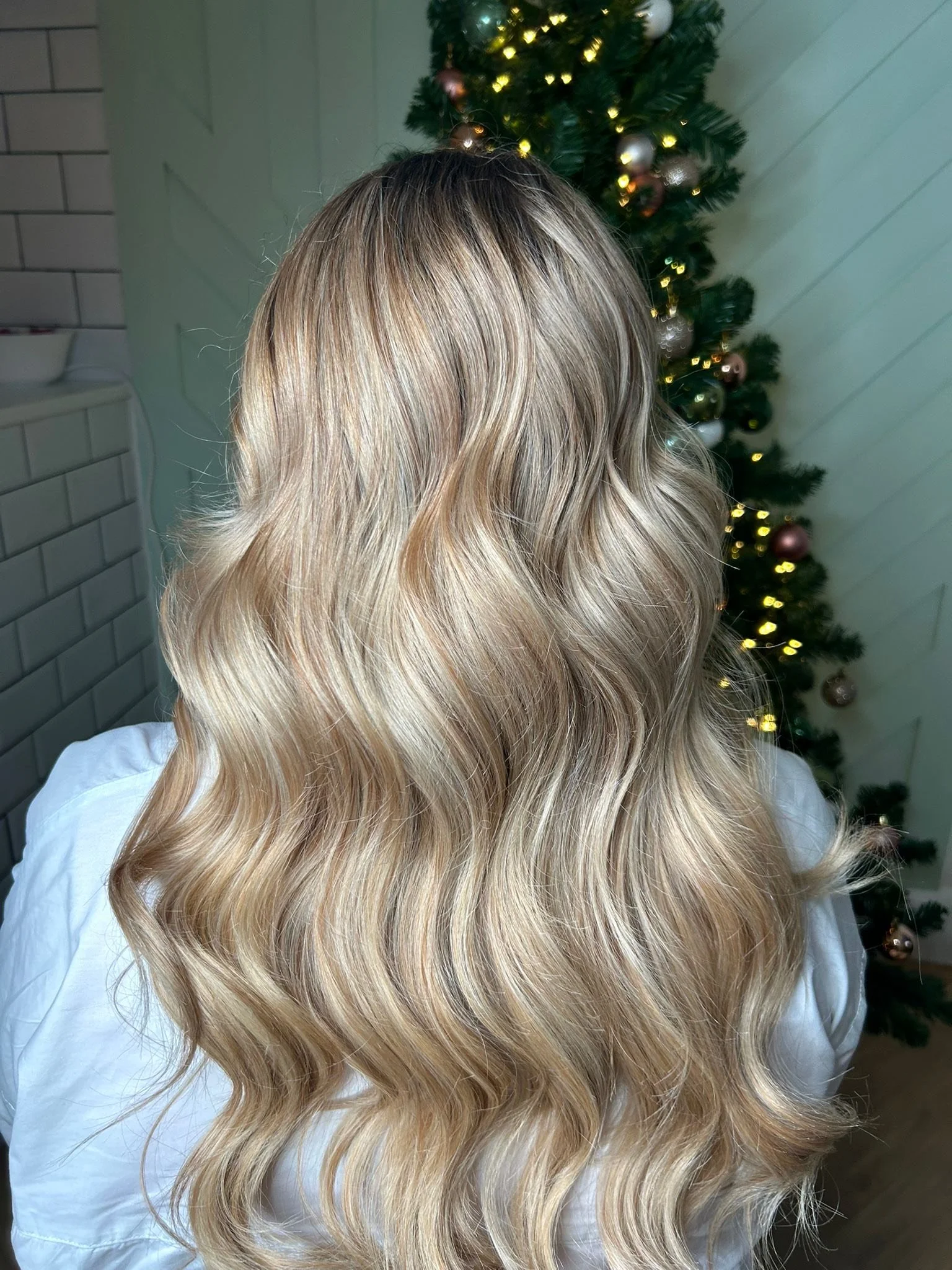 Back view of a woman with long, wavy, blonde hair standing in front of a decorated Christmas tree.