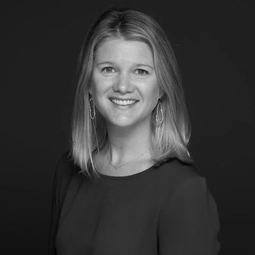 Colby Bishop smiling with shoulder-length hair, wearing earrings and a dark top, against a dark background as secretary and board member of the Photo Ark Foundation