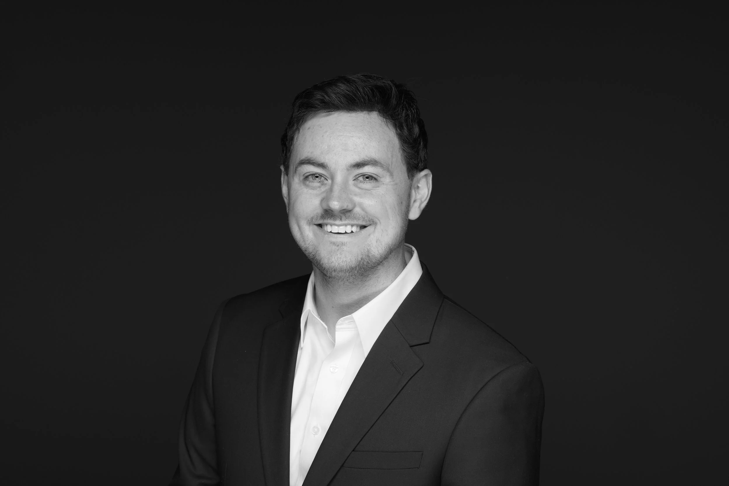 Cole Sartore smiling in a suit and white shirt against a dark background at executive director of the Photo Ark Foundation