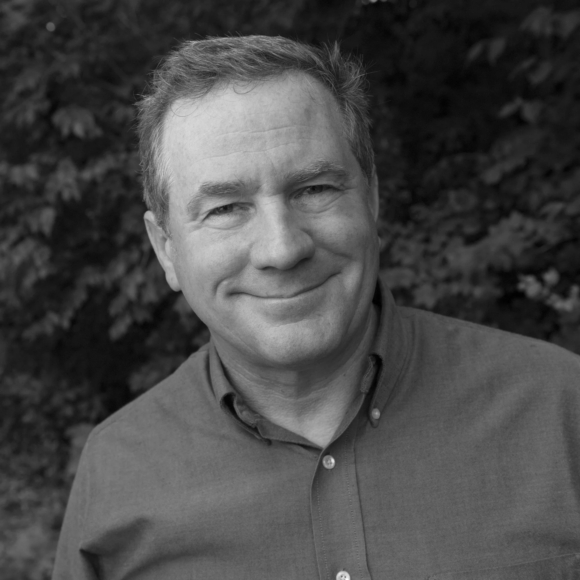 Joel Sartore with short, slightly wavy hair, smiling, outdoors with a background of leaves as board member of the Photo Ark Foundation