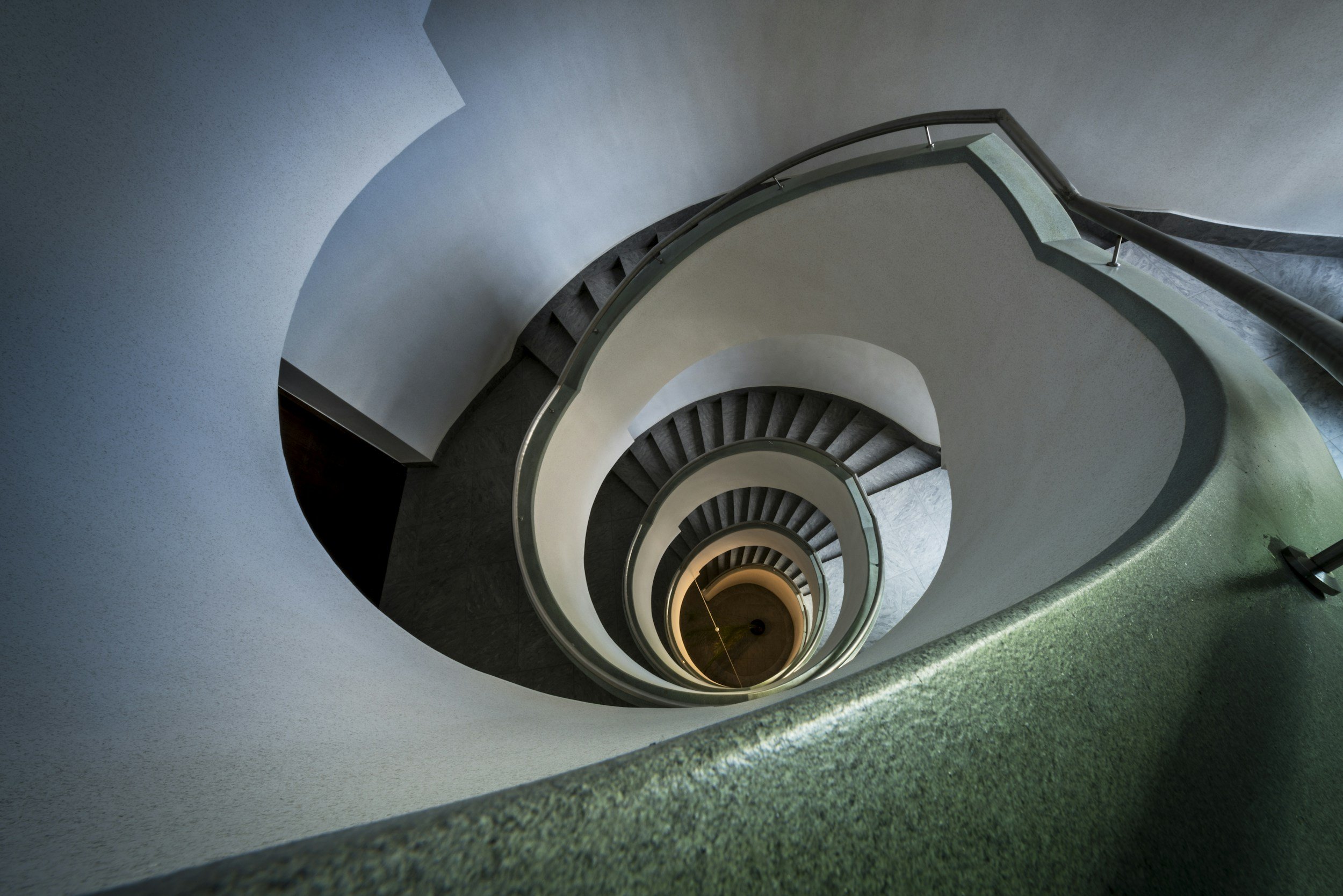 View looking down a spiraling staircase with greenish railing and dark steps, extending downward in a spiral pattern. Breaking negative thought patterns. anxiety spiral down.
