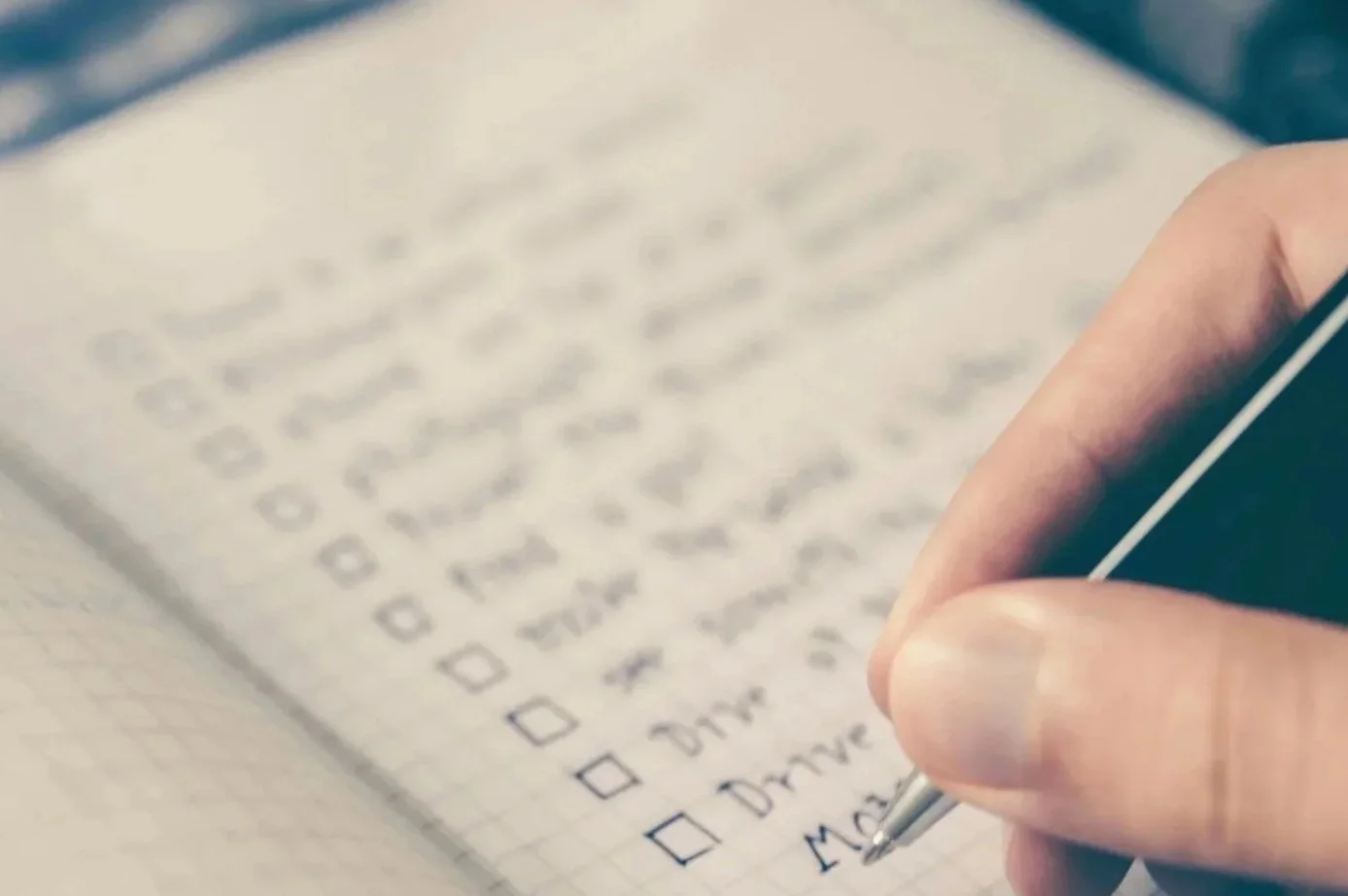 A hand holding a pen and filling out a checklist on a notebook page.