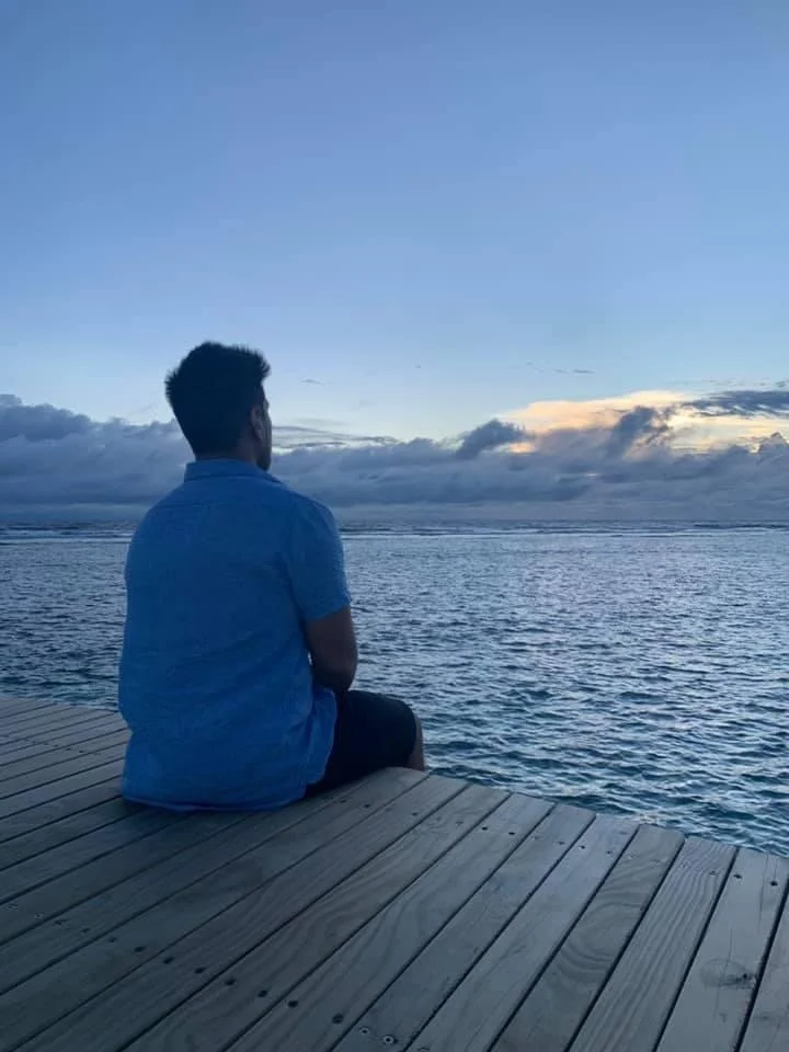 A person sitting on a wooden dock overlooking a body of water during sunset or dusk.