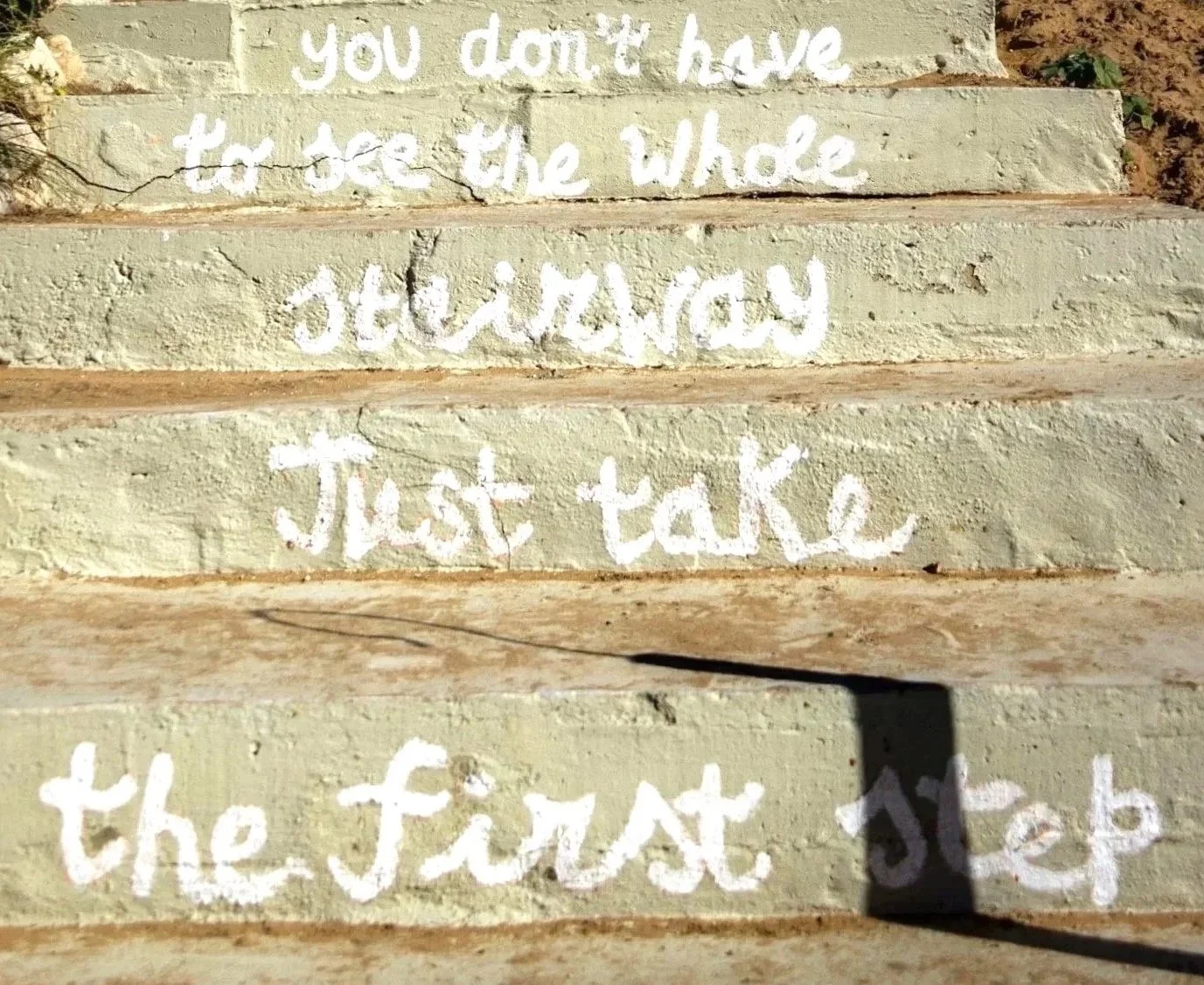 Concrete steps with motivational quote written in white paint: 'You don't have to see the whole staircase, just take the first step.'