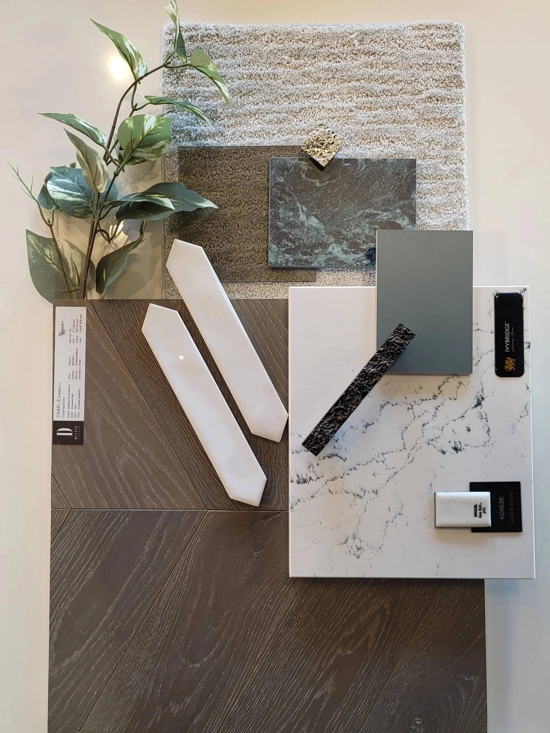 Sample palette with various material samples including marble, wood, and tiles, accented by a green plant and set on a white surface.