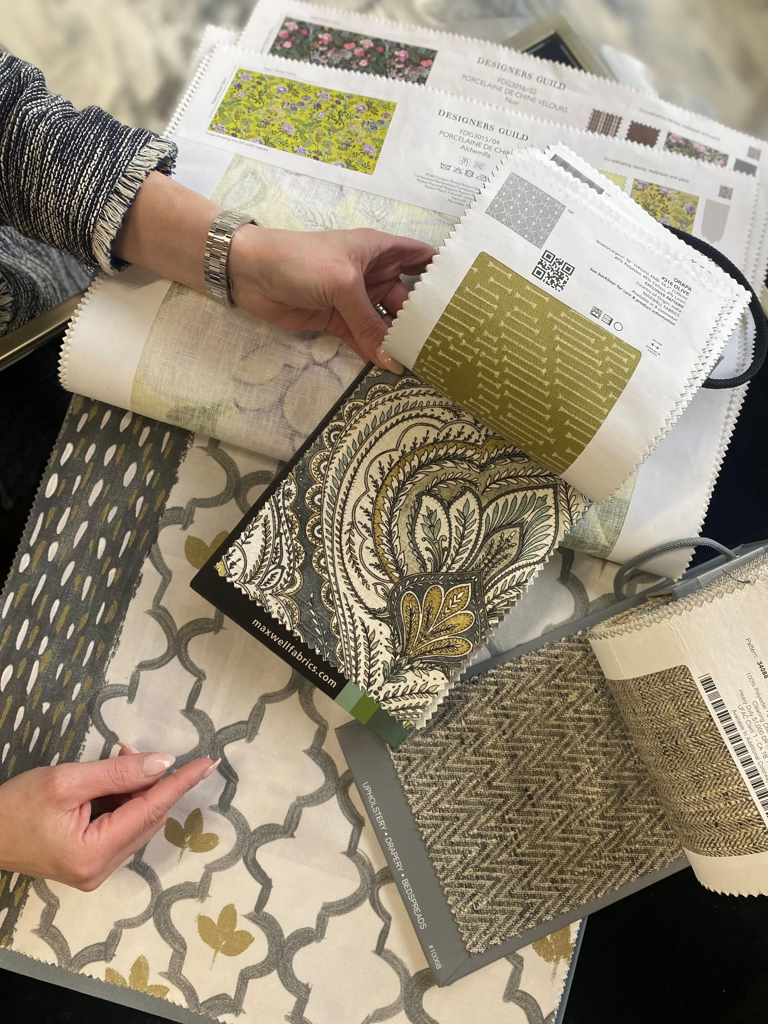 A person holding fabric swatches over a table with more fabric samples and design catalogs.