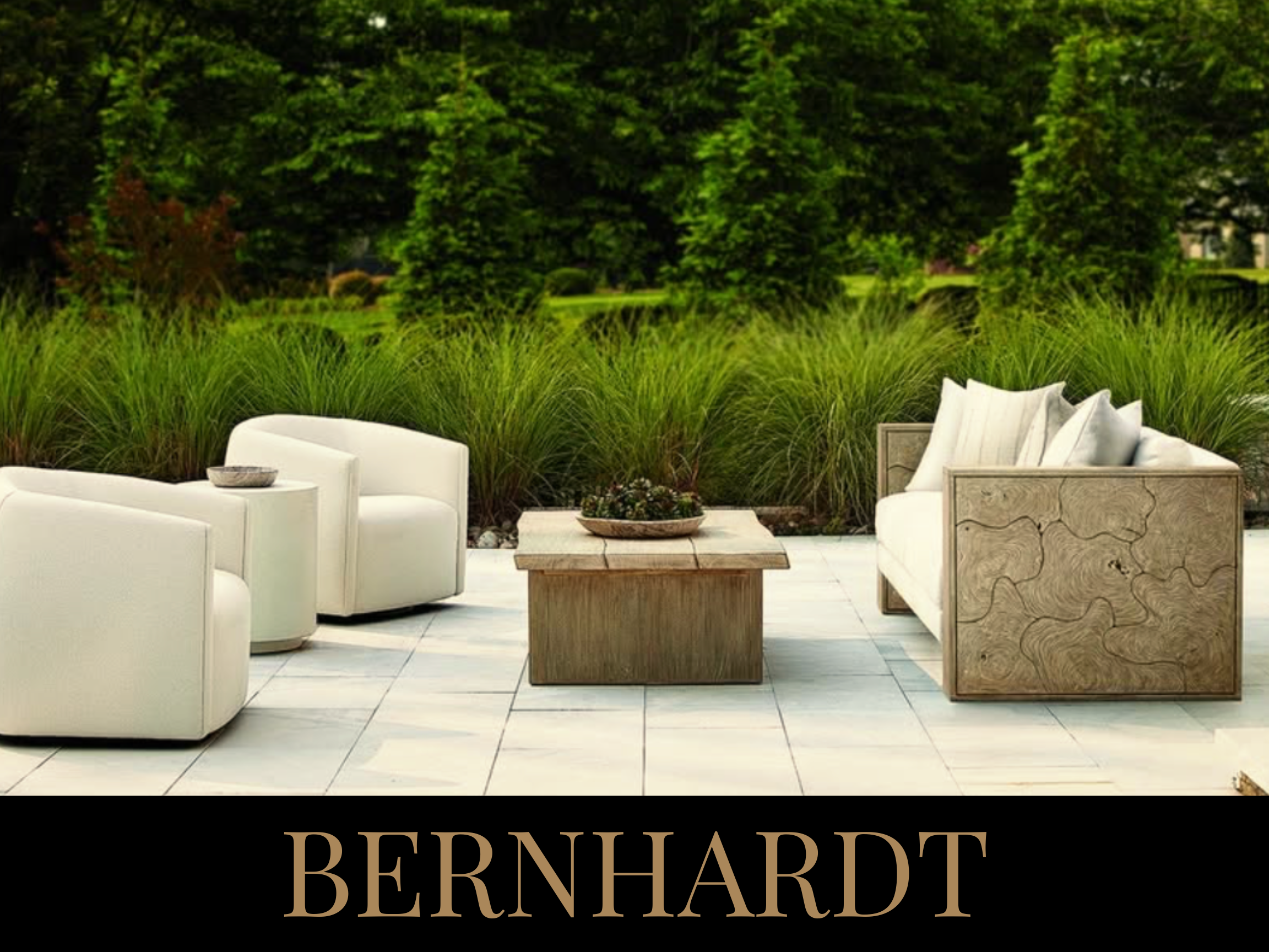 Outdoor patio with white cushioned chairs and a sofa, wooden coffee table, surrounded by greenery, with the word BERNHARDT below.