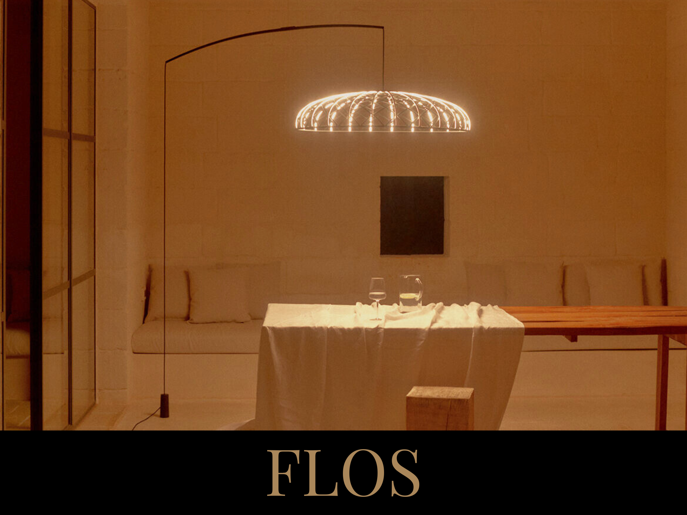 A minimalist dining room with a wooden table, beige seating, a hanging light fixture, and a black wall art piece.