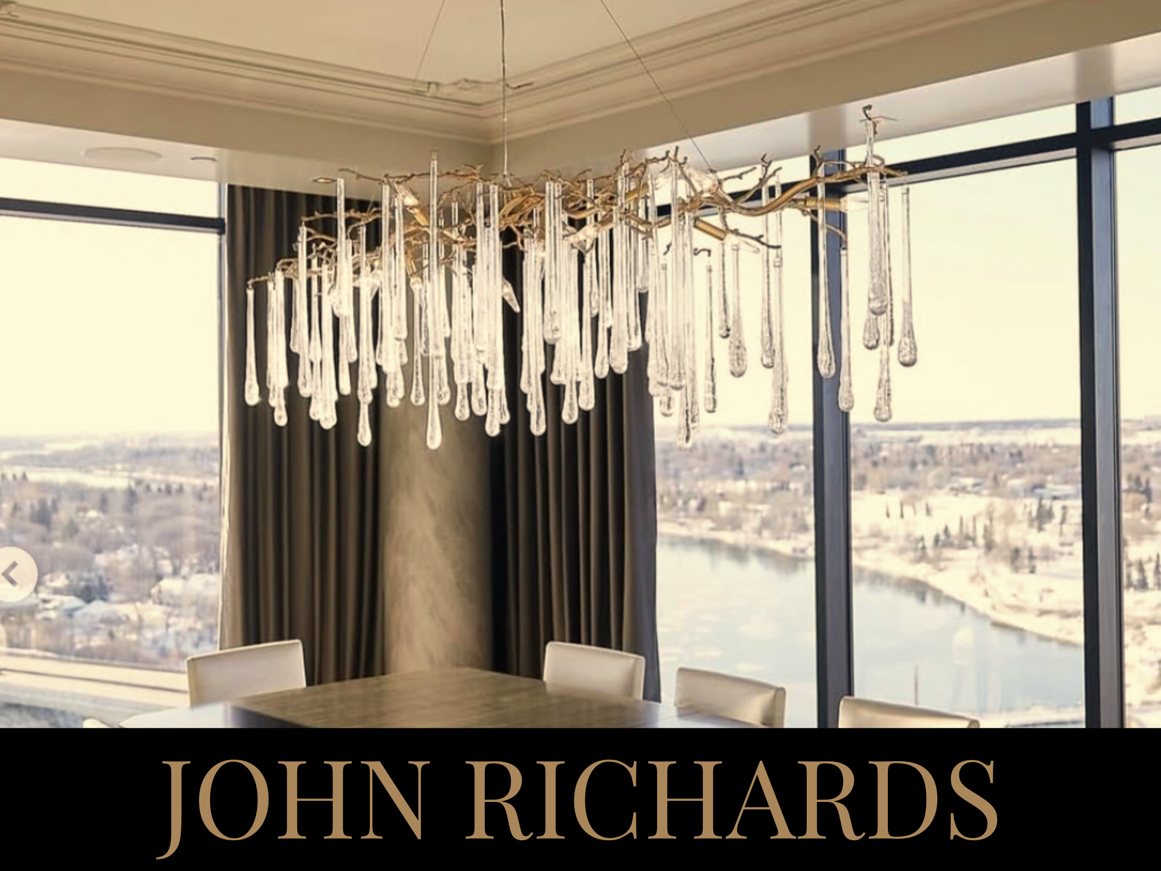 Elegant chandelier with glass droplets hanging inside a room with large windows and cityscape view.
