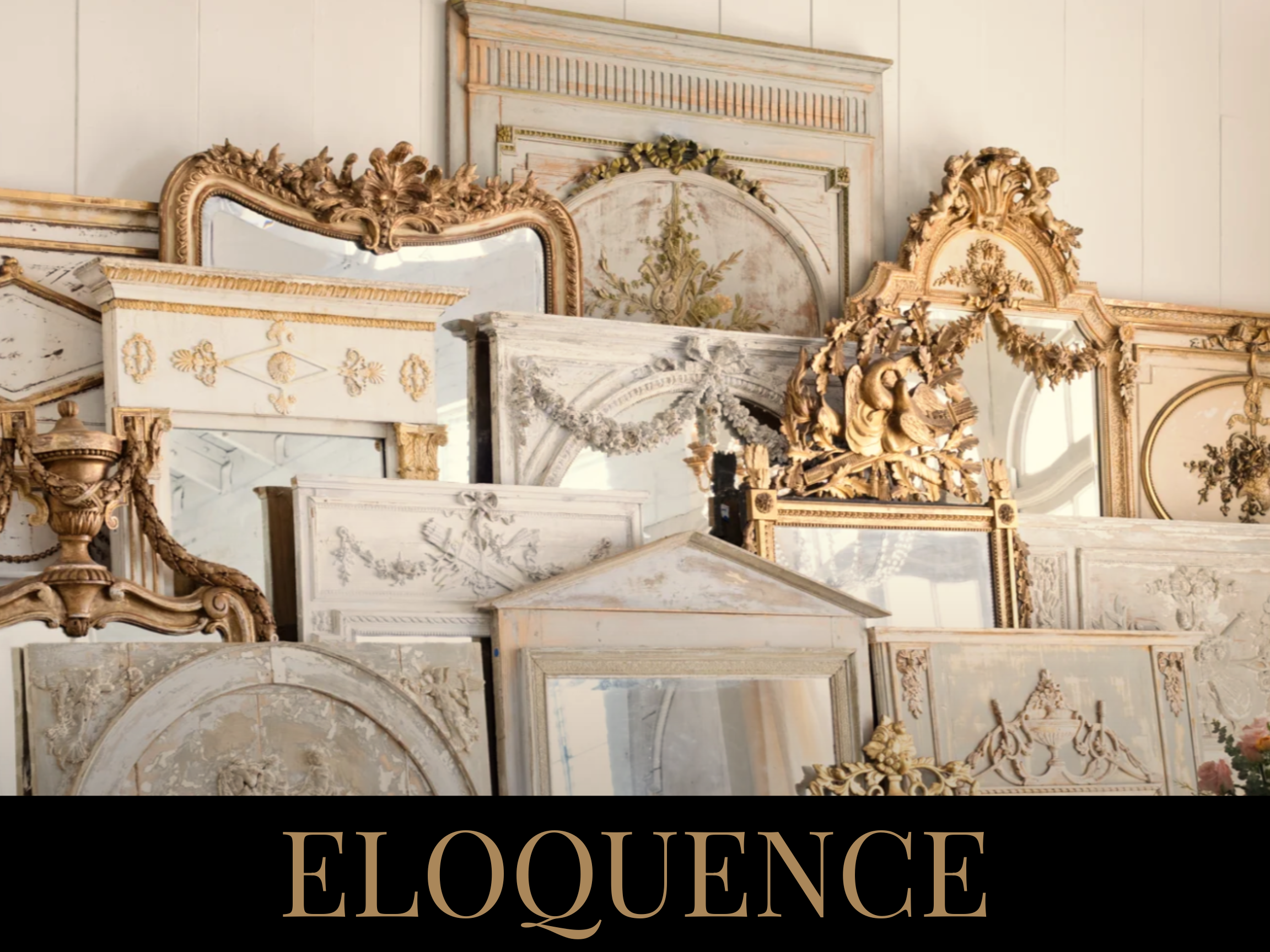 A collection of antique mirrors and picture frames with ornate and carved designs, stacked against a wall. The frames are in shades of white, cream, and gold, with some featuring floral and decorative motifs.