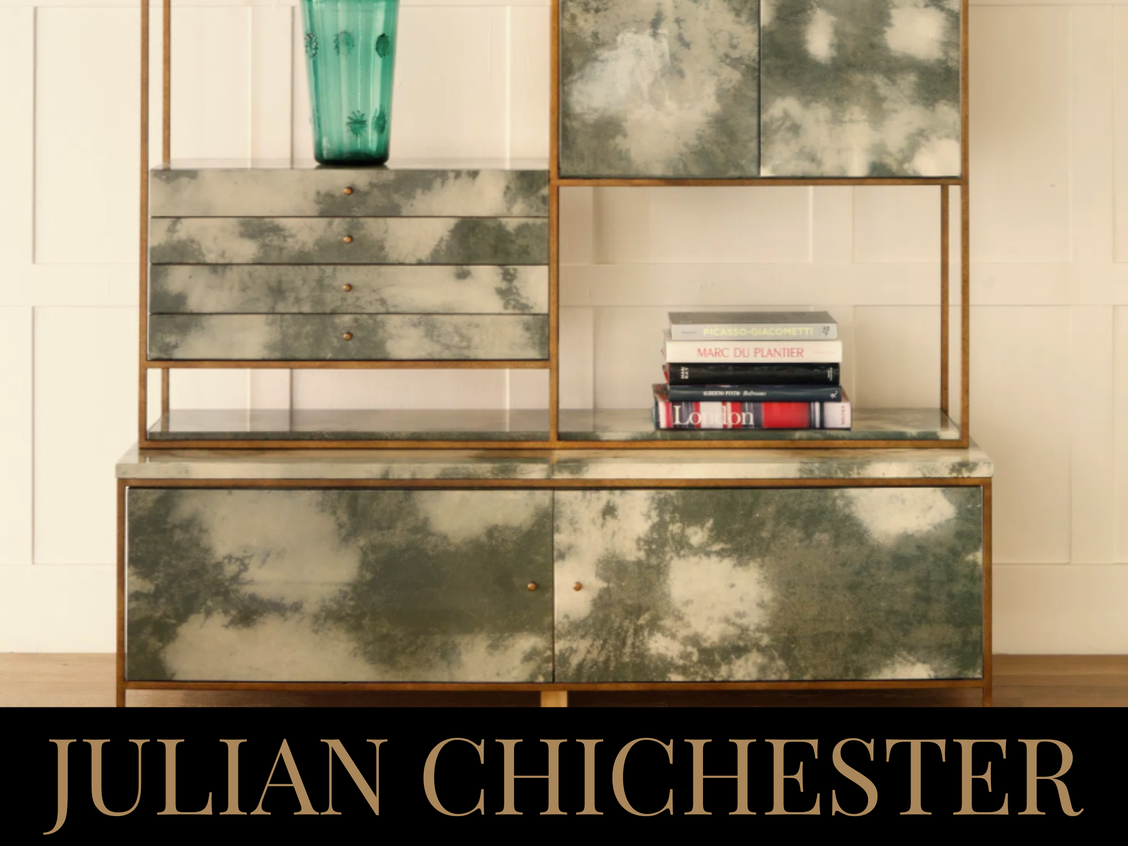 A vintage nightstand featuring a green textured drawer unit with wood frame and brass knobs, topped with a large green glass vase, and a lower cabinet with two doors. Above, a shelf holds a small stack of books, with white tile walls in the backgroun