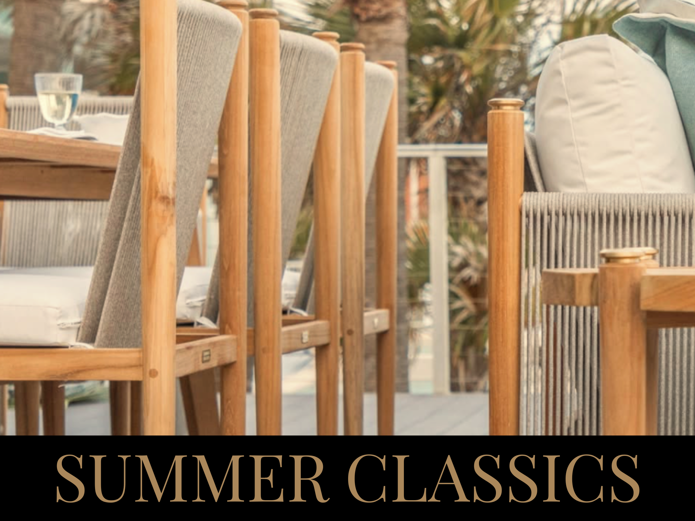 Close-up of outdoor wooden chairs with beige cushions and a patio dining table with a glass of water, with plants and patio furniture in the background