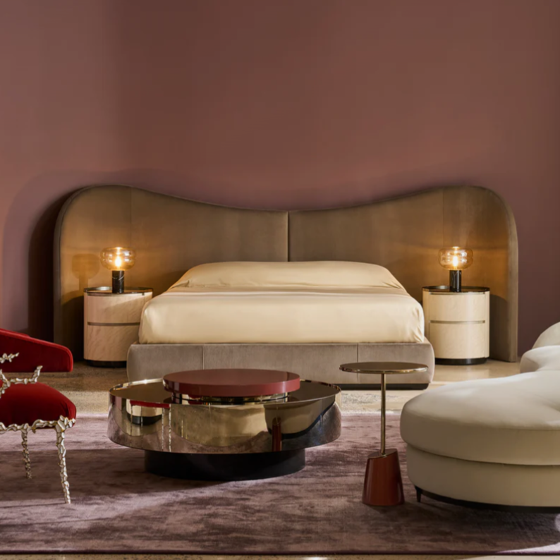 Elegant bedroom with a large bed, curved wooden headboard, and soft lighting from stylish lamps on nightstands, complemented by modern furniture and a plush purple area rug.