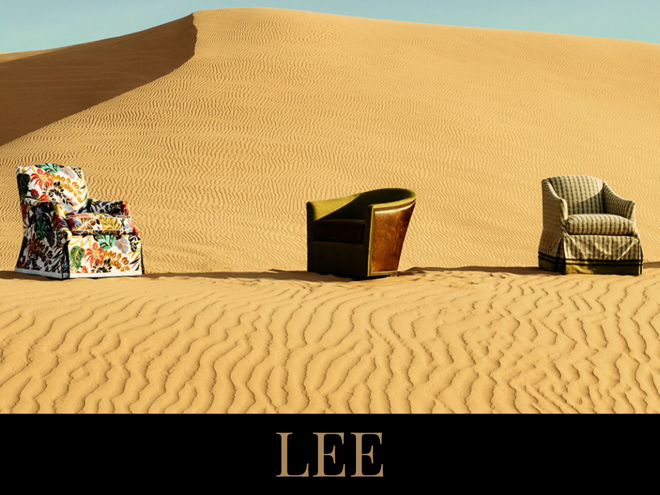 Three chairs placed on sand dunes in a desert with a clear sky, with the name "LEE" at the bottom
