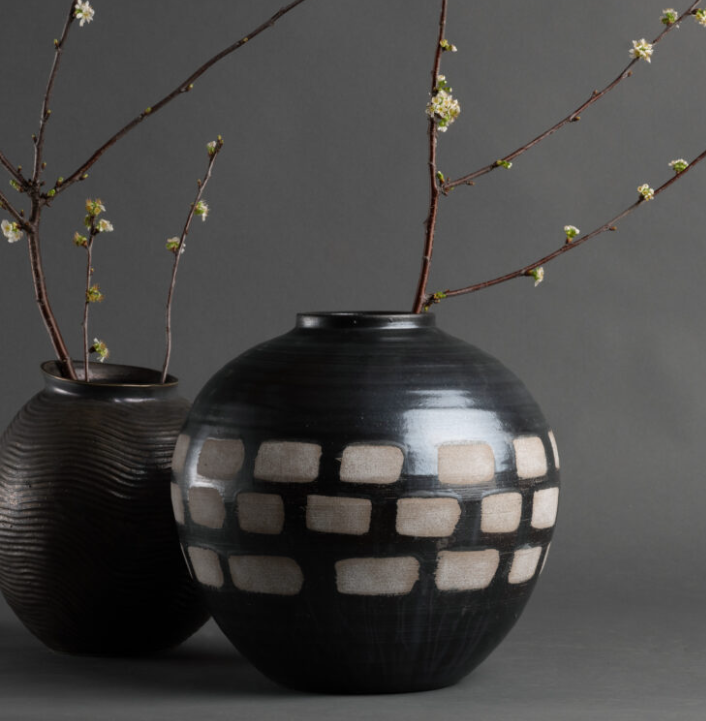 Two black vases with brown branches and small white flowers on a gray surface against a gray background.