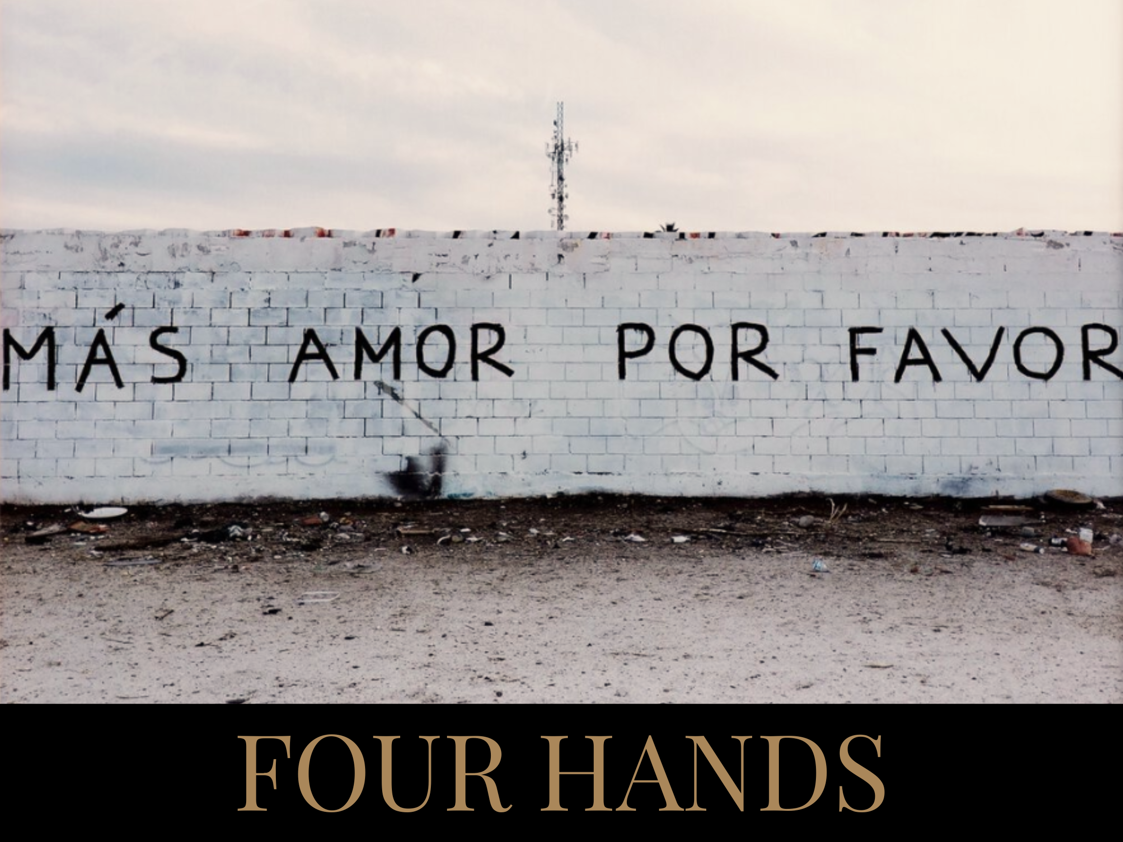 White brick wall with Spanish text 'MÁS AMOR POR FAVOR' painted on it, and the words 'FOUR HANDS' in gold lettering on a black background below.