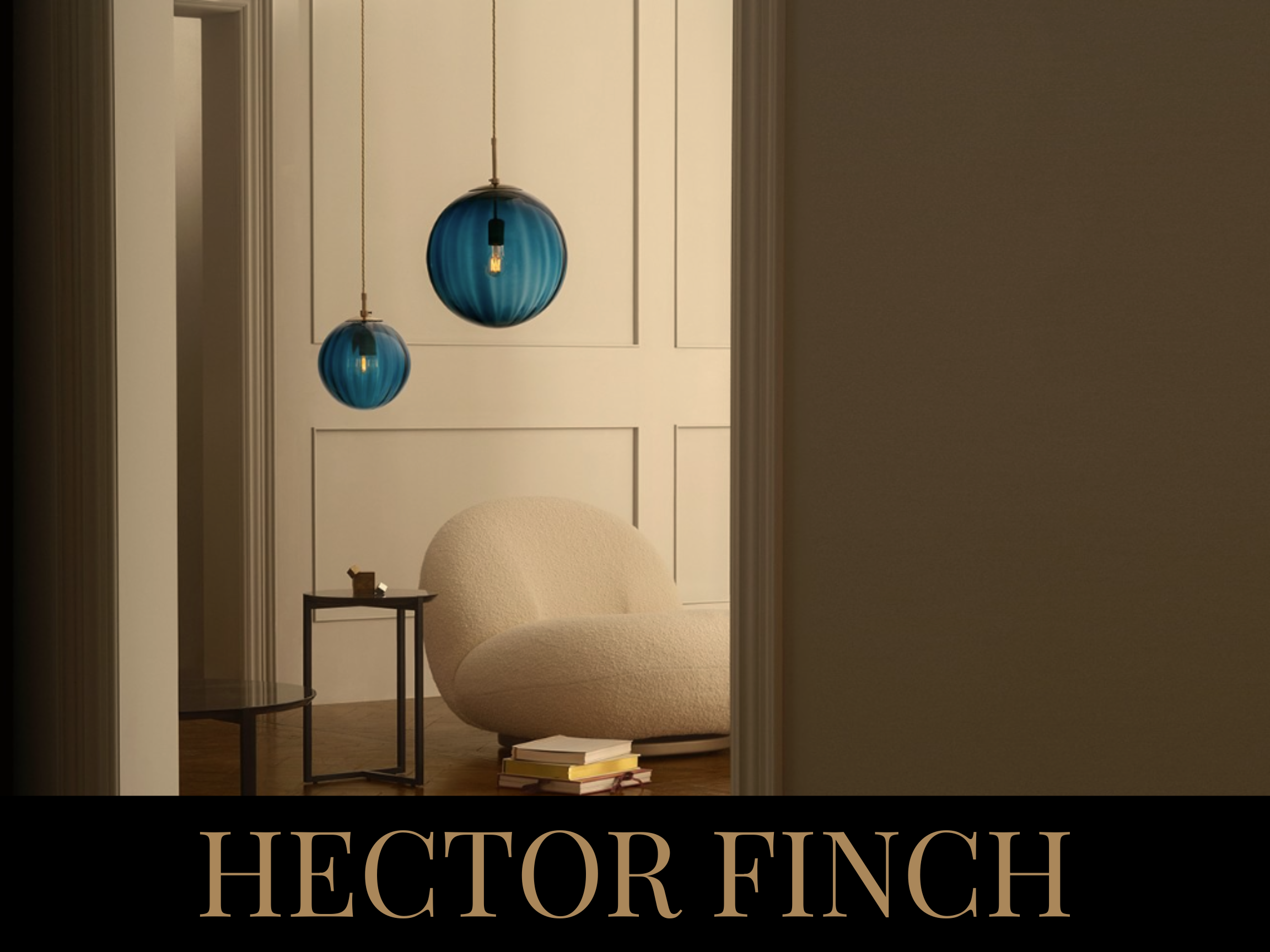 A cozy sitting area with a rounded, cream-colored armchair, a small black side table, and two blue pendant lights hanging from the ceiling against a white paneled wall.