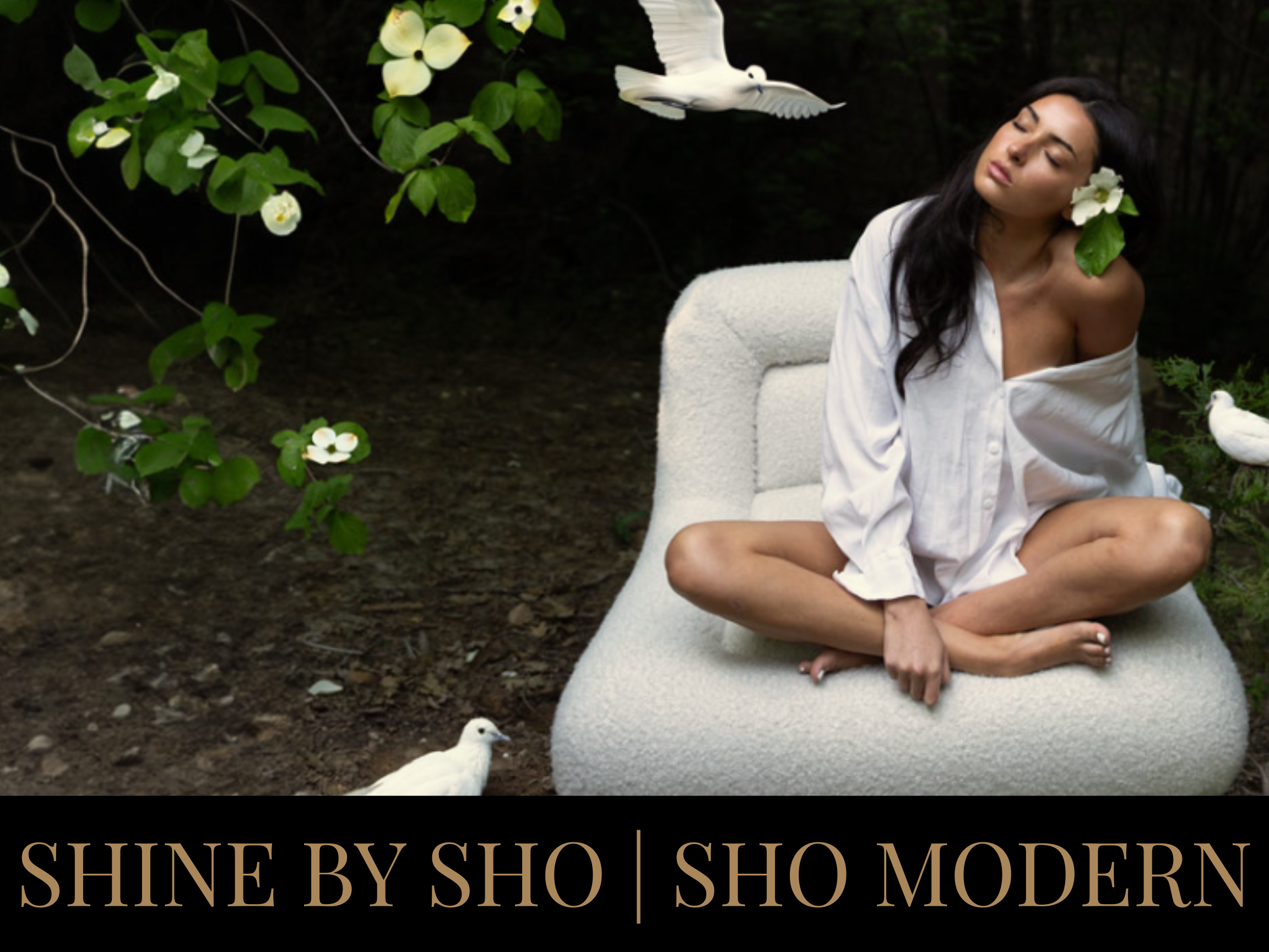 A woman with long dark hair, sitting cross-legged on a white cushioned seat outdoors, wearing a white off-shoulder shirt, with white flowers in her hair and around her. White birds are flying and perched nearby, with green foliage and flowers in the 