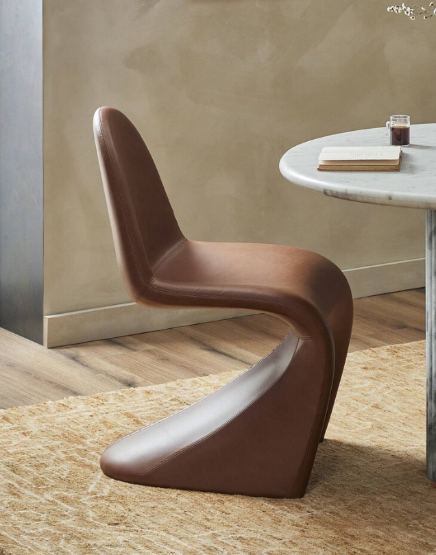 A modern brown leather chair next to a white marble table with a glass of dark beverage and a closed book on it.