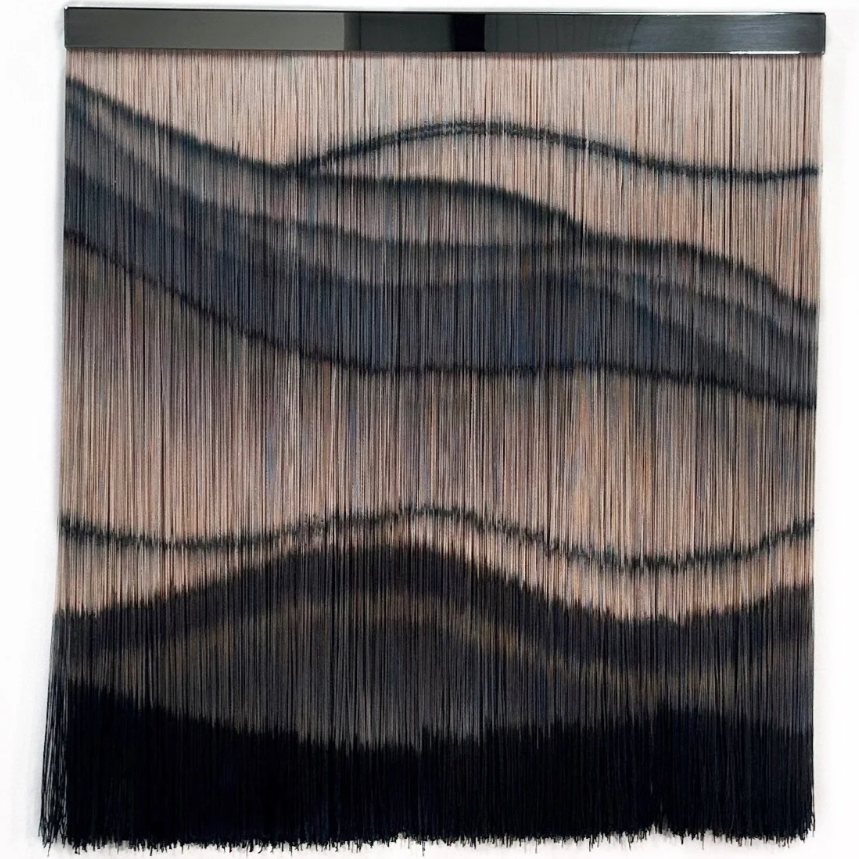 A decorative wall hanging with black, brown, and beige wavy lines on a textured beige background.