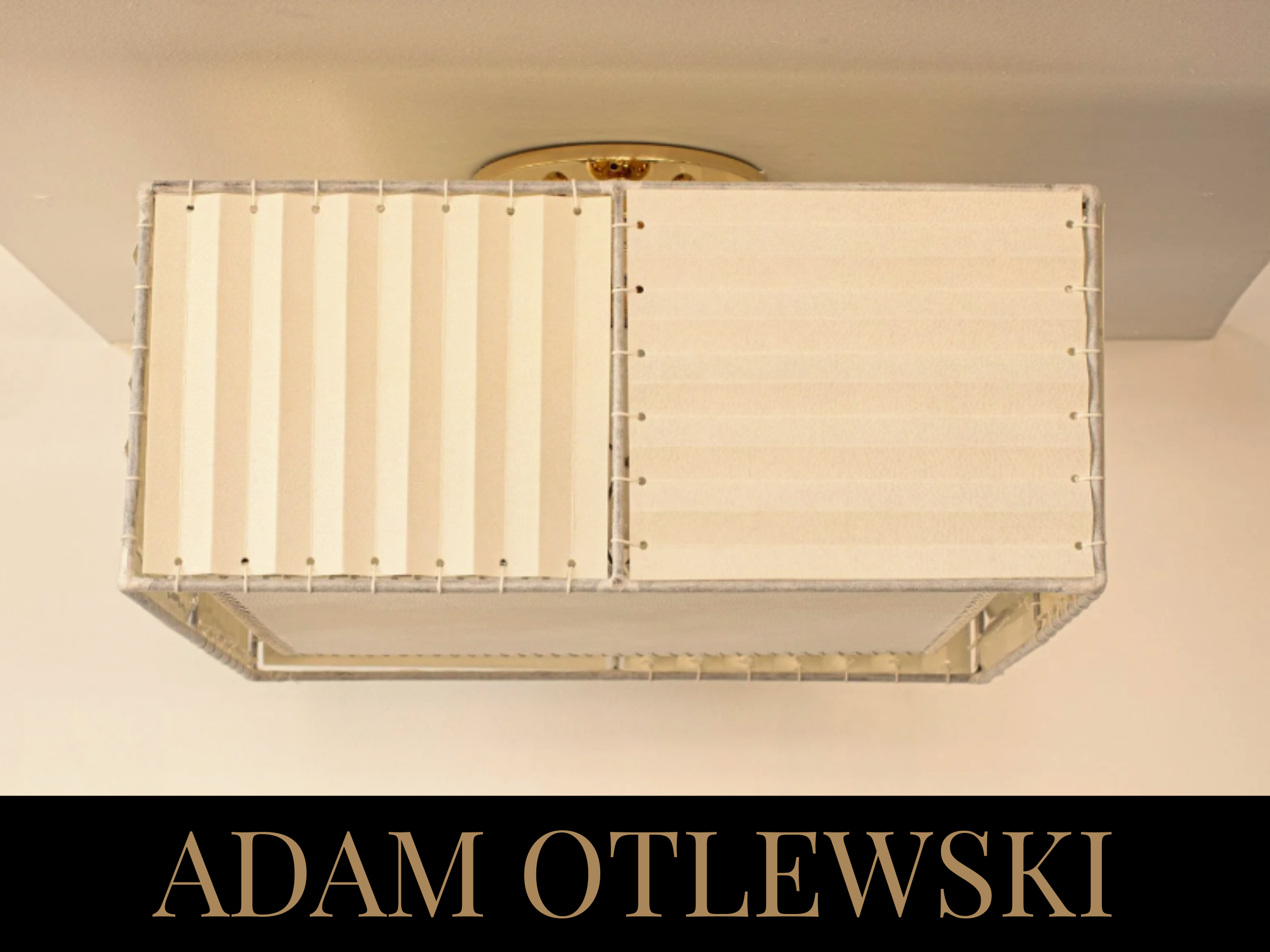 A modern ceiling light fixture with a rectangular white shade, featuring vertical and horizontal lines, mounted on a white ceiling. The bottom of the image displays the name "ADAM OTLEWSKI" in large beige letters on a black background.