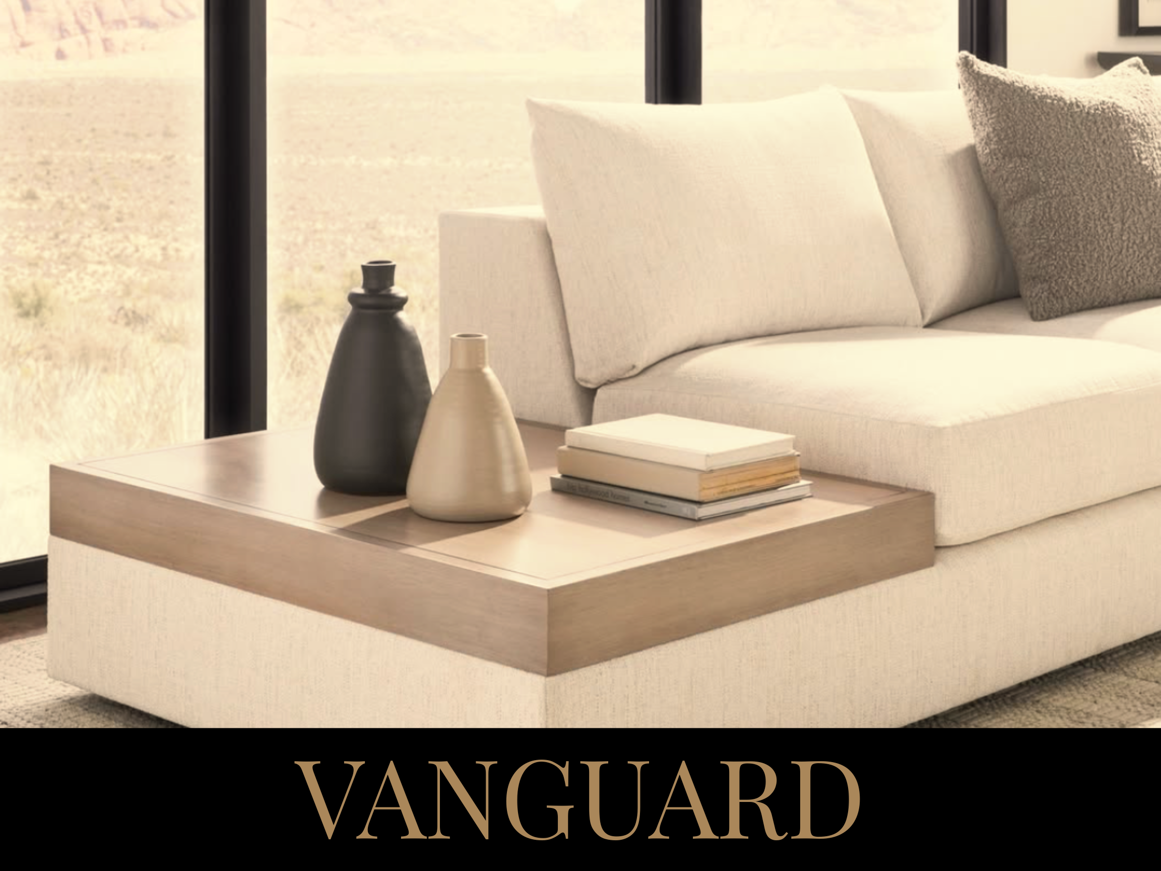 Modern living room with beige sofa, decorative pillows, and a wooden coffee table with vases and books, large window with a desert landscape outside, and the word "VANGUARD" displayed at the bottom.