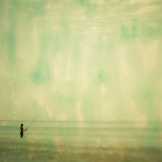 A person fishing alone on a vast, calm body of water with a reflective, slightly greenish surface.