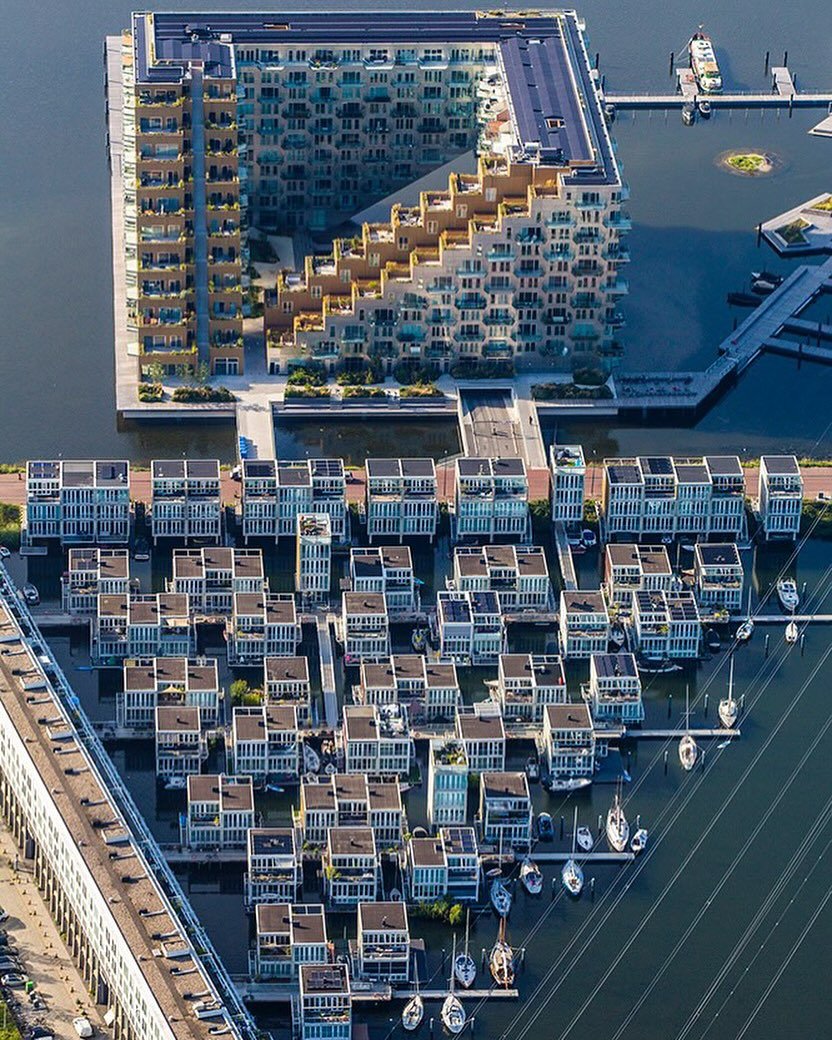 FLOATING HOMES AFFORDABLE STUDENT FAMILY HOUSING Aerial view of a waterfront residential area with a mix of high-rise apartments and townhouses, some with boat docks and sailboats in the water.