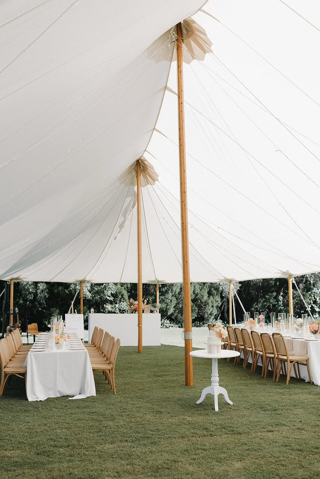 Elegant outdoor wedding reception under a large white tent with long tables, chairs, and floral centerpieces.