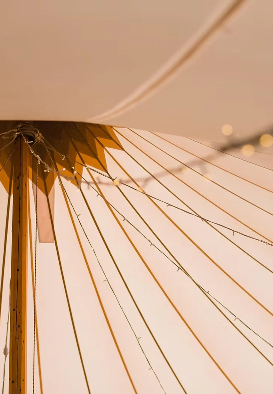 Close-up of a beige and orange striped beach umbrella with small string lights attached.