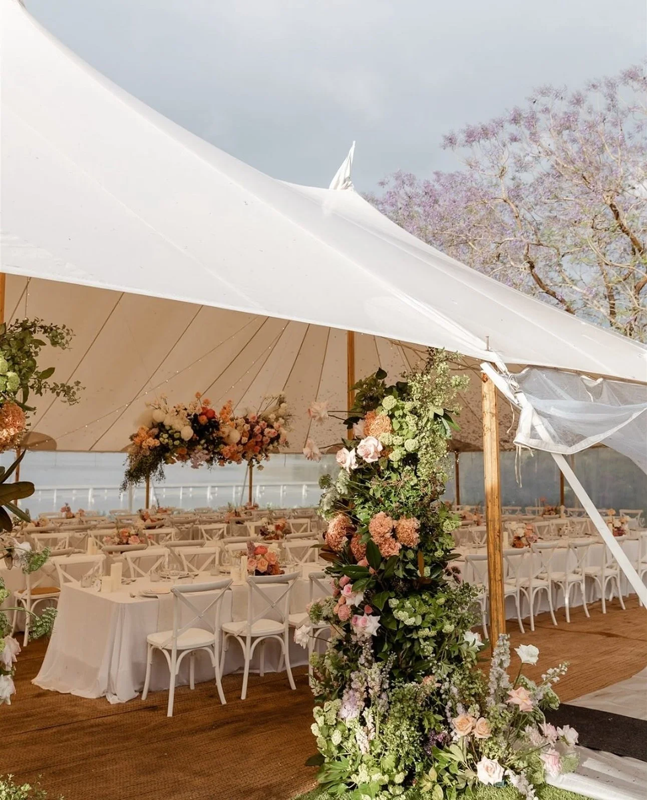 Decorative wedding reception setup inside a white tent with floral arrangements, tables, and chairs.