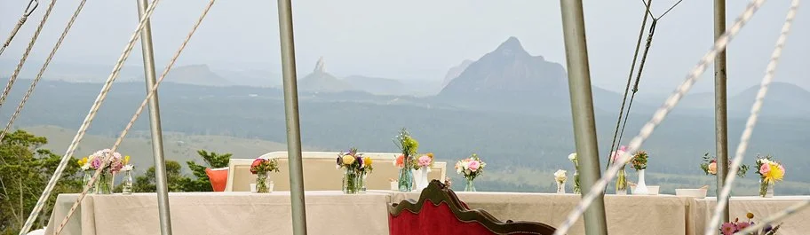An outdoor dining table set with flower arrangements, with a mountain and forest landscape in the background.