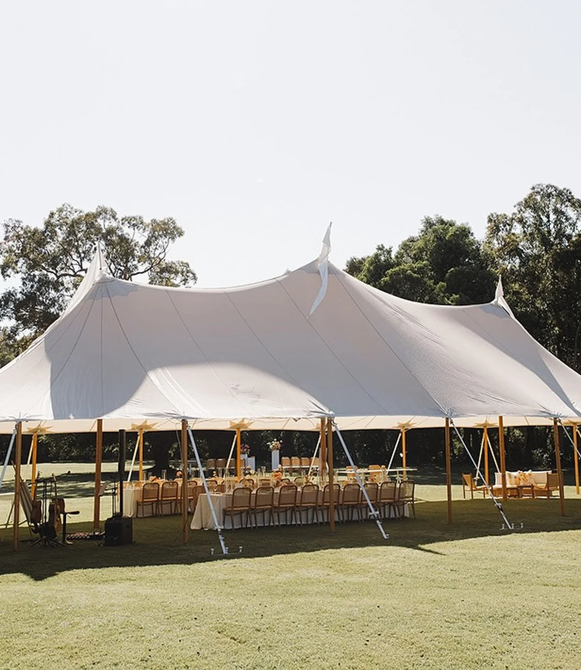 Large white event tent set up outdoors on a grassy field under clear sky, with chairs and tables arranged inside for a gathering.