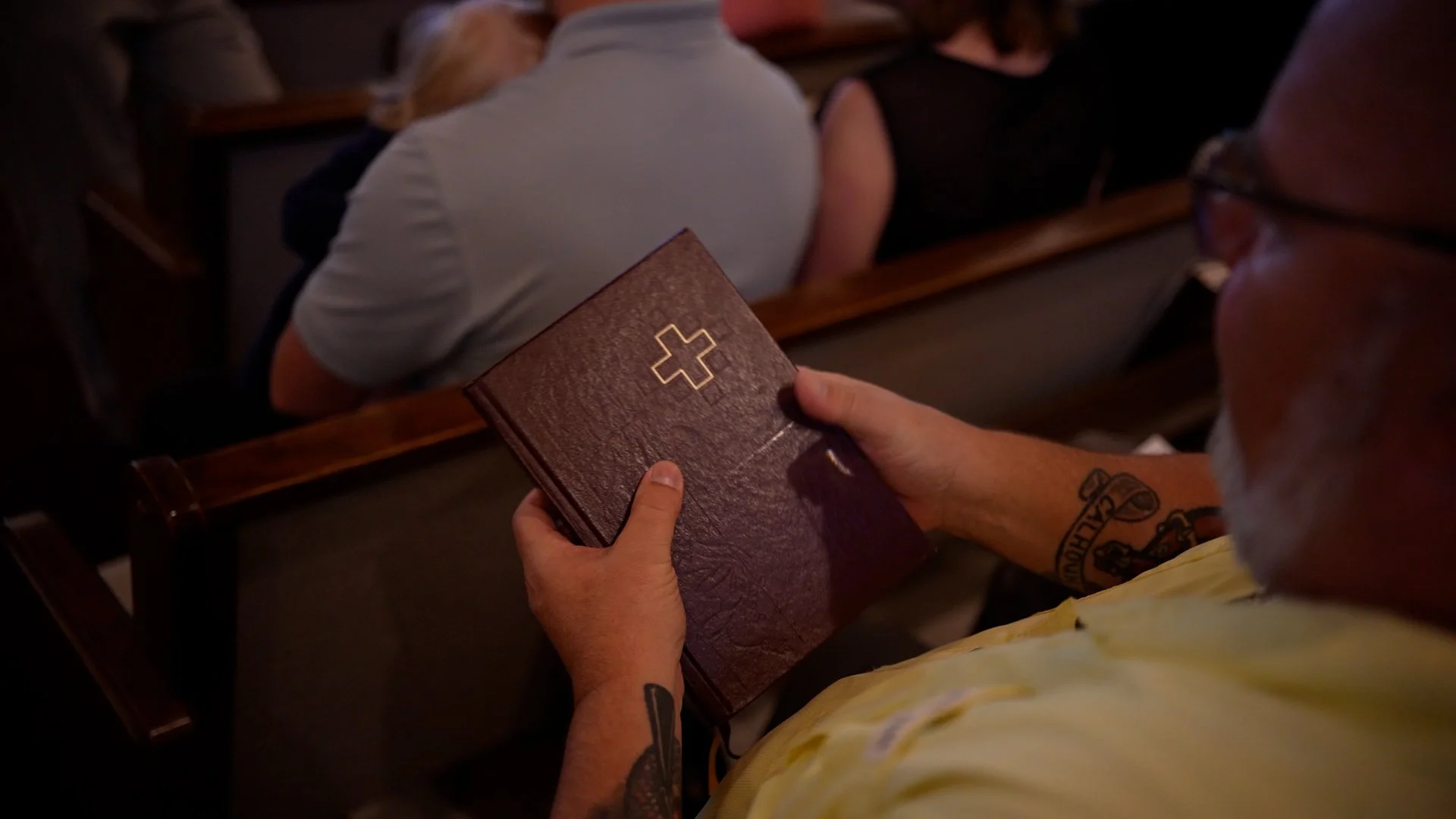 A worshipper holding a Bible with a gold cross on the cover during a Sunday service at Redeemer Lutheran Church in Olathe, Kansas, engaged in prayer and reflection.