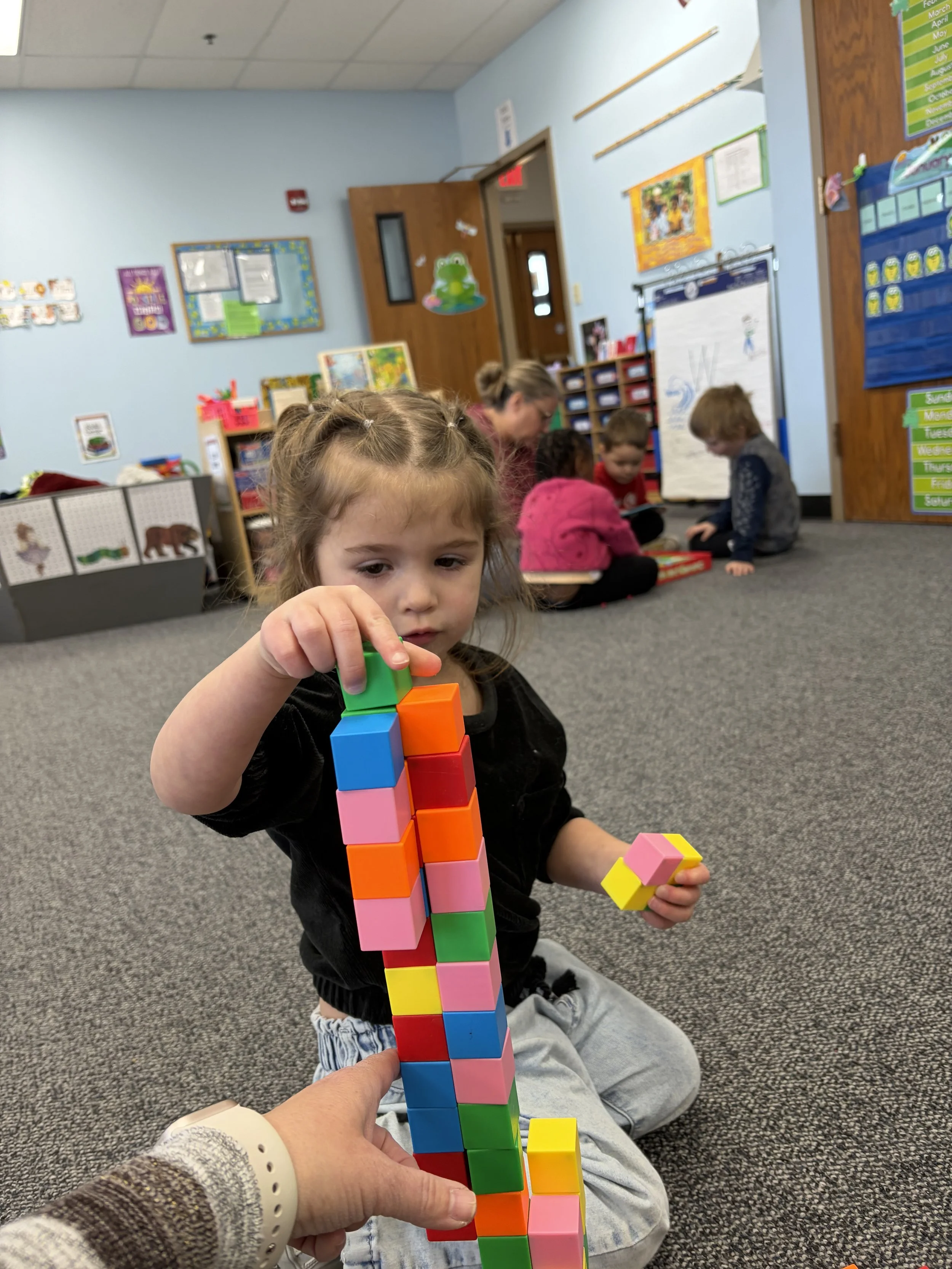 A young child at Redeemer Lutheran Preschool in Kansas City carefully stacking colorful blocks to build a tall tower, highlighting hands-on learning and creative play.