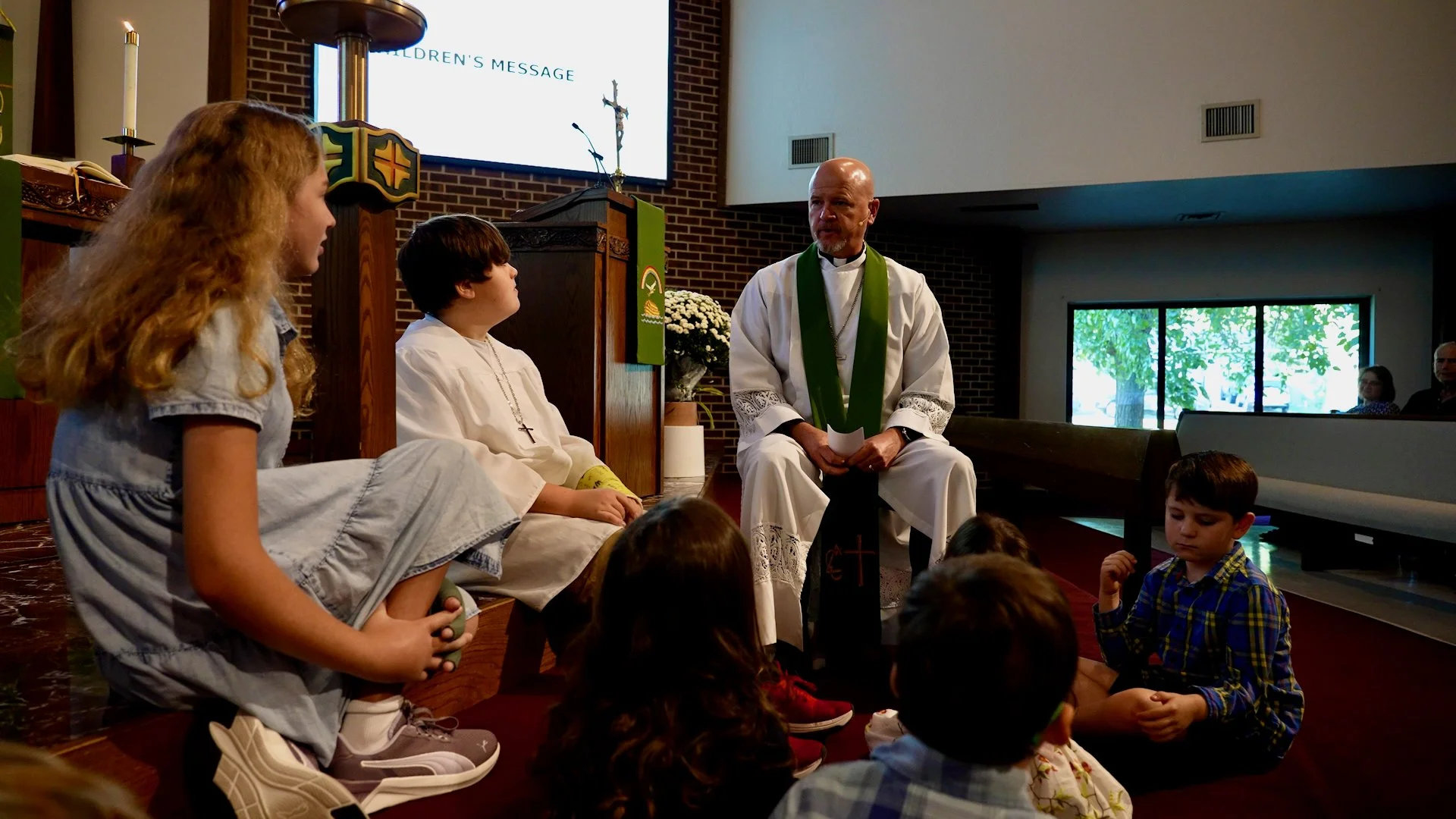 Pastor Kahle leading a children’s message at Redeemer Lutheran Church in Olathe, Kansas, engaging young members in faith and teaching inside the sanctuary.