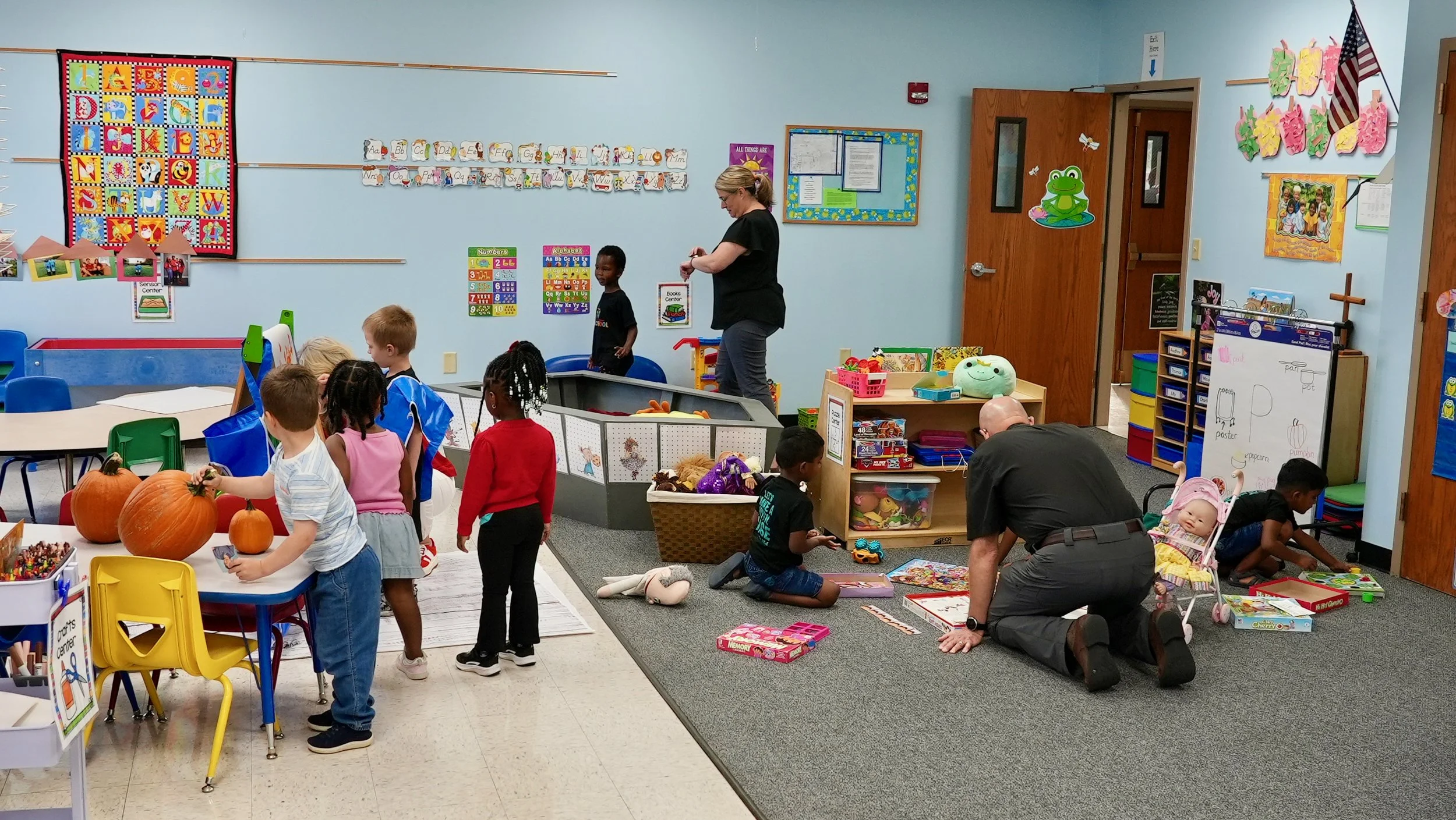 Preschool classroom at Redeemer Lutheran Preschool in Olathe, Kansas, with children and teachers engaged in learning activities, pumpkins on the table, colorful decorations, and educational materials on the walls.