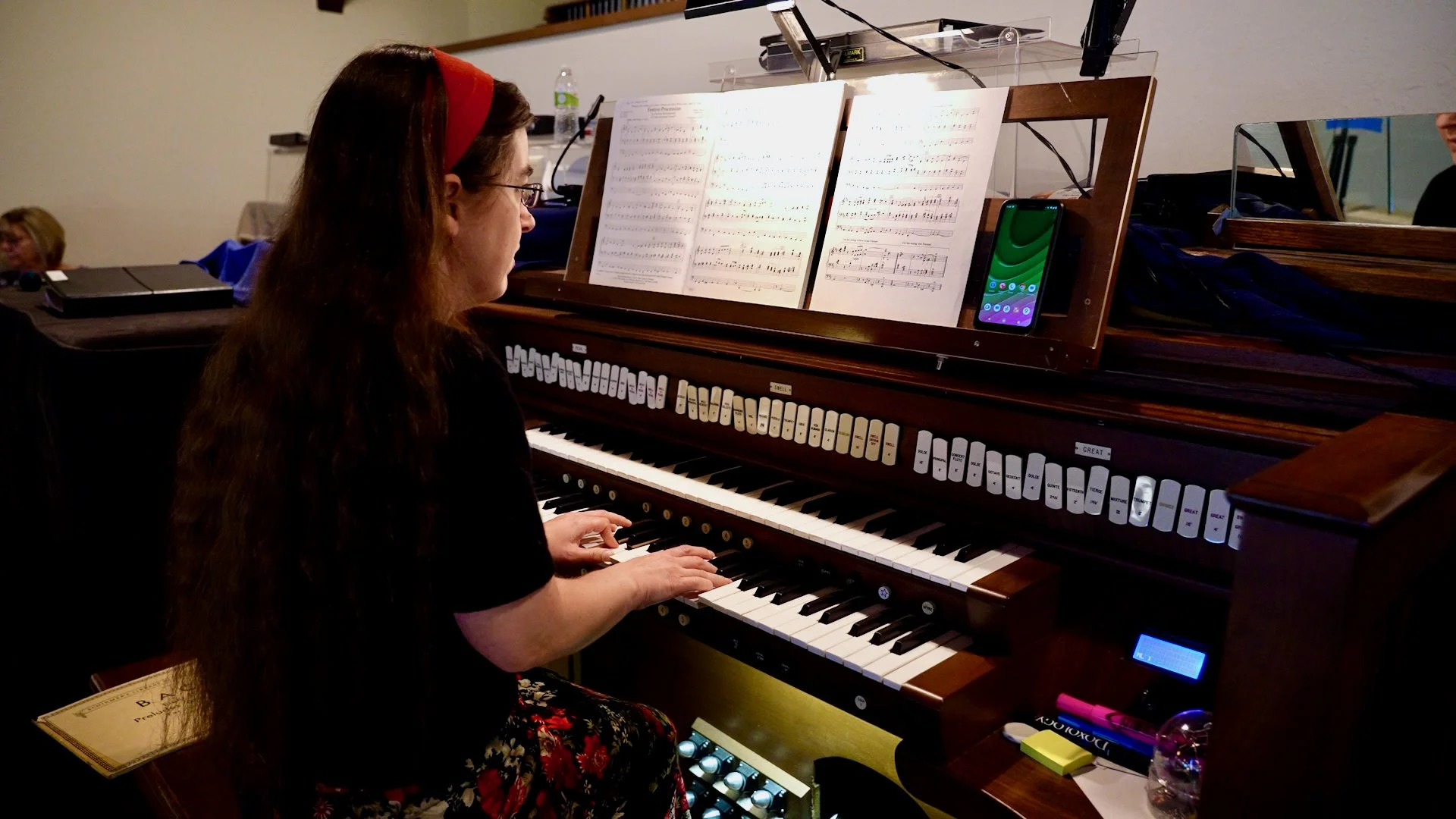 A musician playing the organ during Redeemer Lutheran Church’s Classic Praise Service on Sunday, with sheet music on the stand, a smartphone nearby, and personal items on the organ.