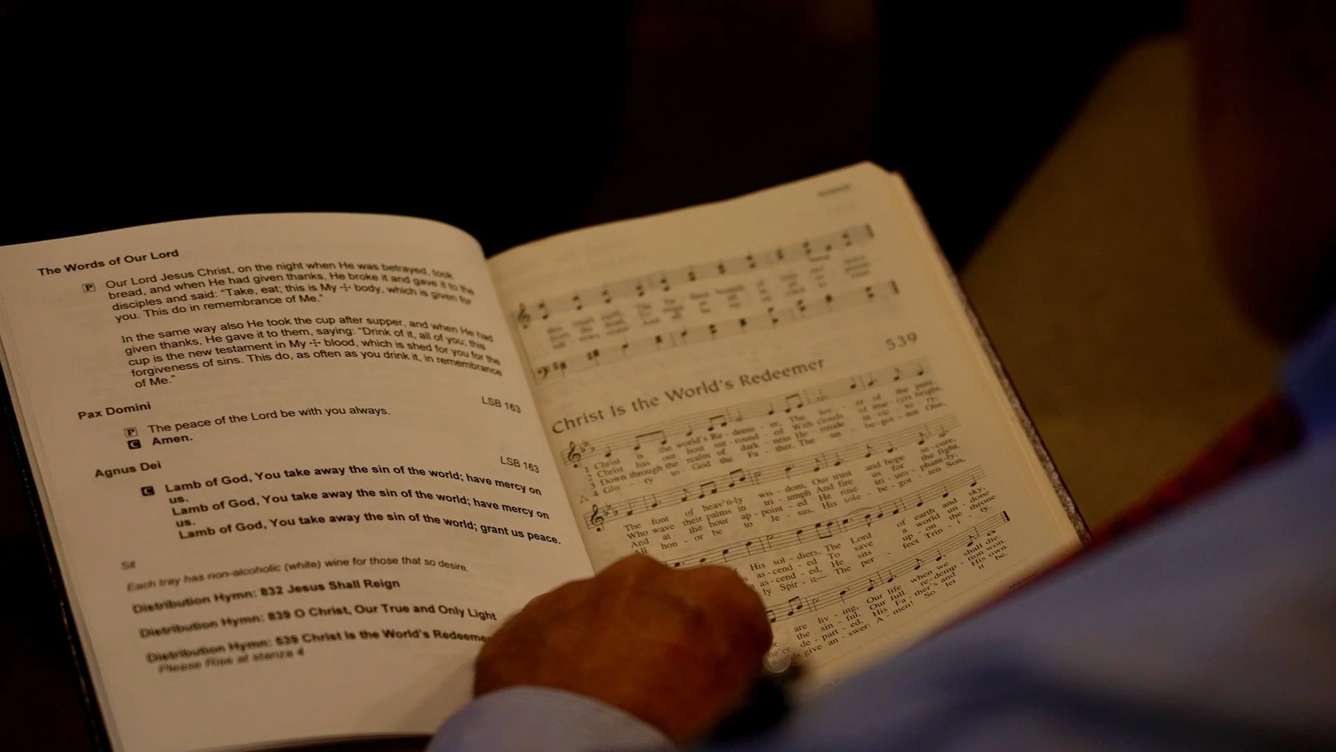 Worshipper at Redeemer Lutheran Church holding a hymnal open to ‘Christ Is the World’s Redeemer,’ reflecting on the song during a service in the sanctuary.