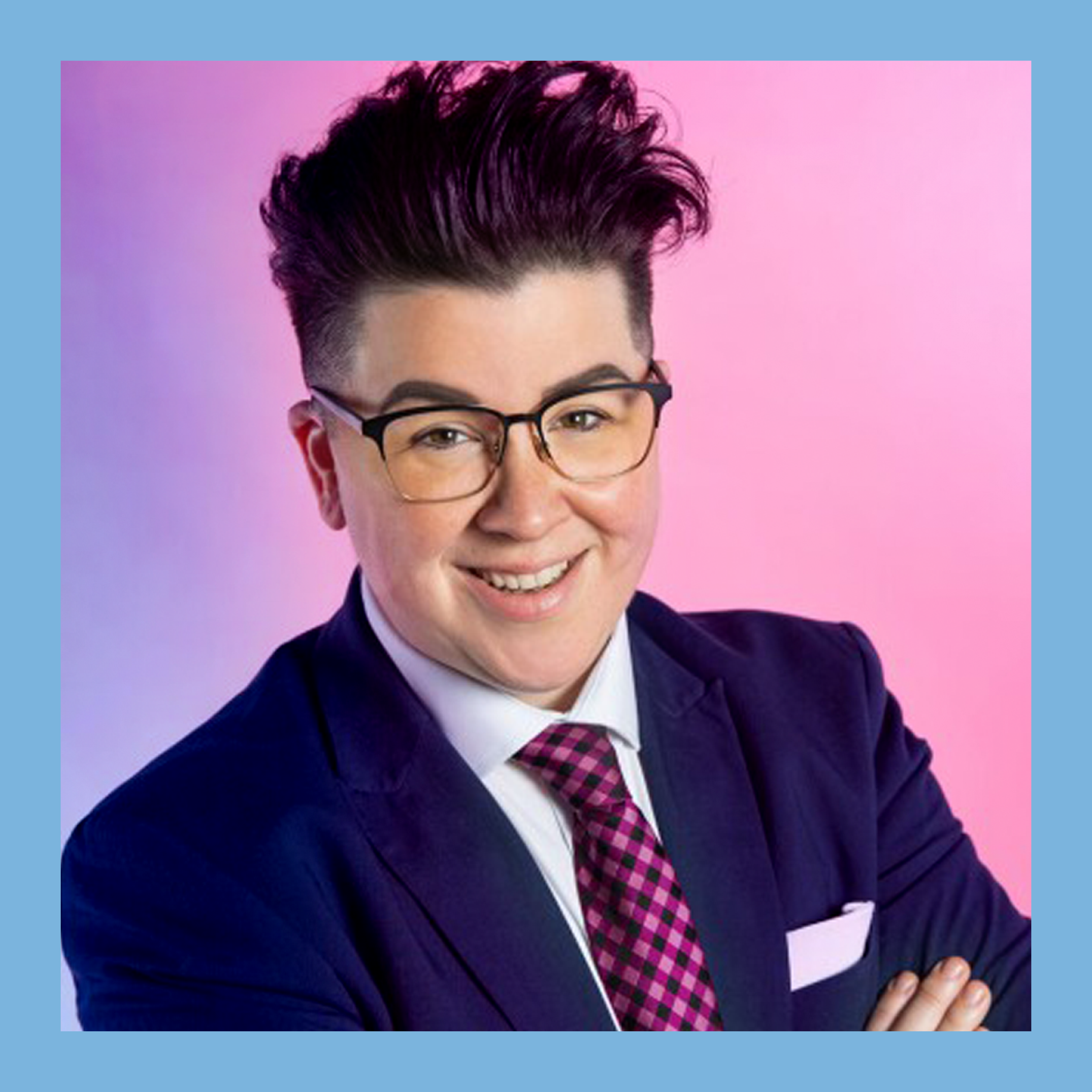 Young person with styled dark hair, wearing glasses, a navy blazer, a white shirt, and a pink checkered tie, smiling against a pink and purple gradient background.